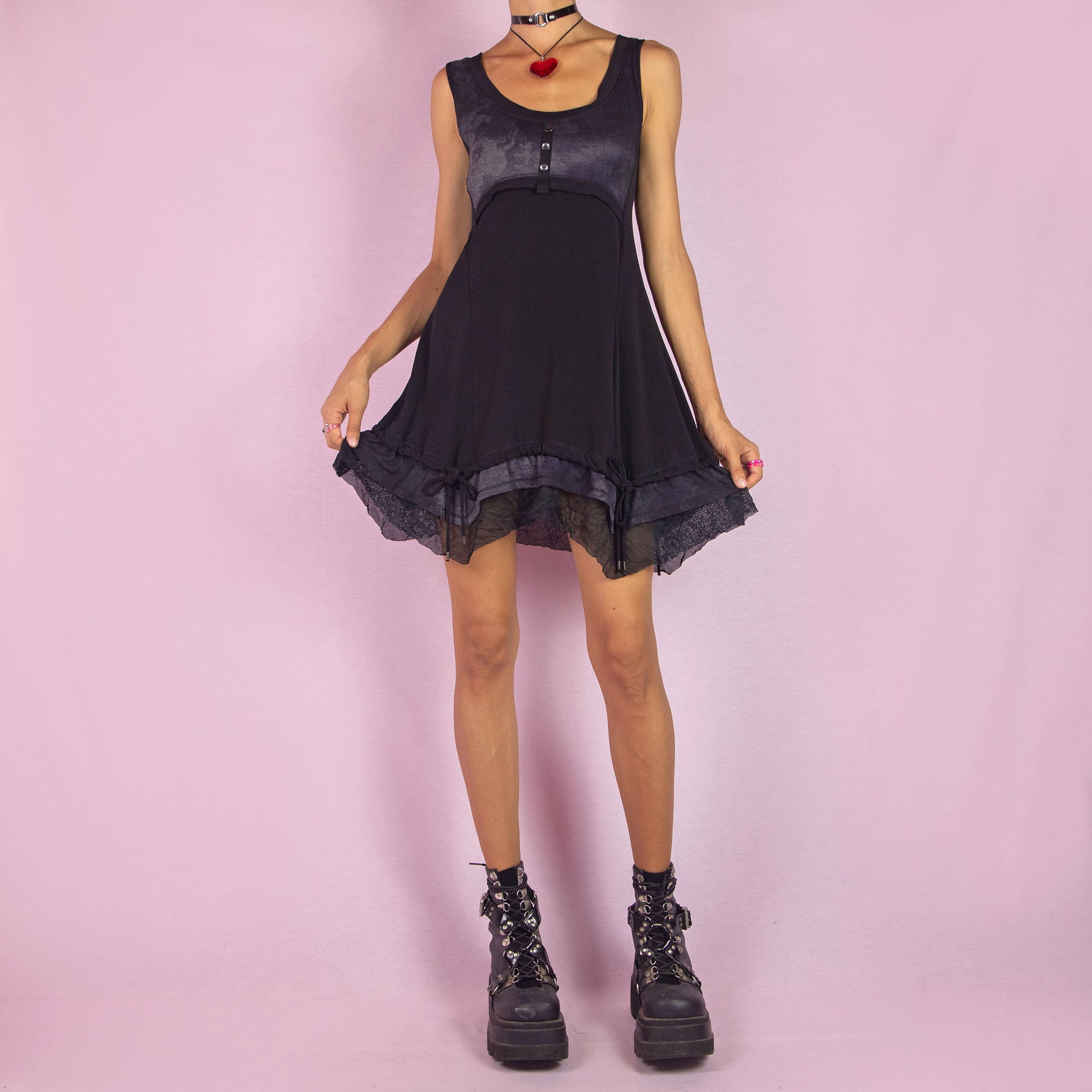 The Y2K Sleeveless Black Mini Dress is a vintage 2000s piece featuring a sleeveless design with a scoop neckline. Made from stretchy fabric, this dress has a buttoned bodice detail and a subtle tie-dye print across the top. The layered ruffle hem with mesh accents and adjustable drawstring ties adds a customizable fit. Perfect for summer casual outings or night parties.