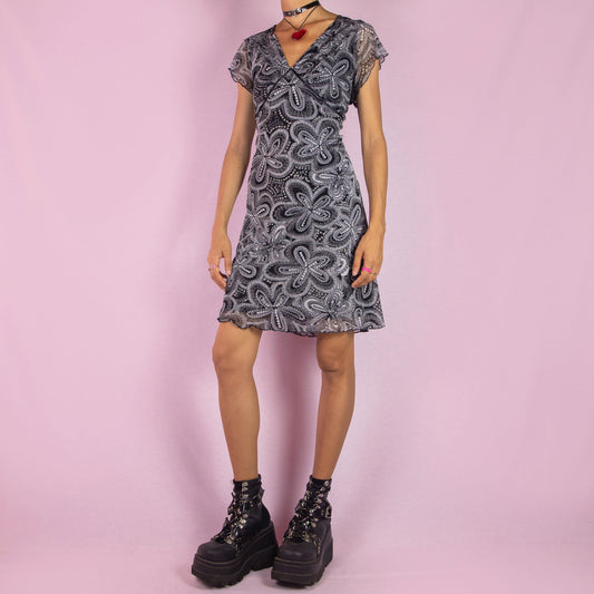 The Y2K Mesh Printed Mini Dress is a vintage 2000s piece featuring a sheer mesh fabric with an abstract floral print. This dress has a V-neckline, cap sleeves, and a fitted silhouette. Perfect for summer wear, casual outings, or a night out.