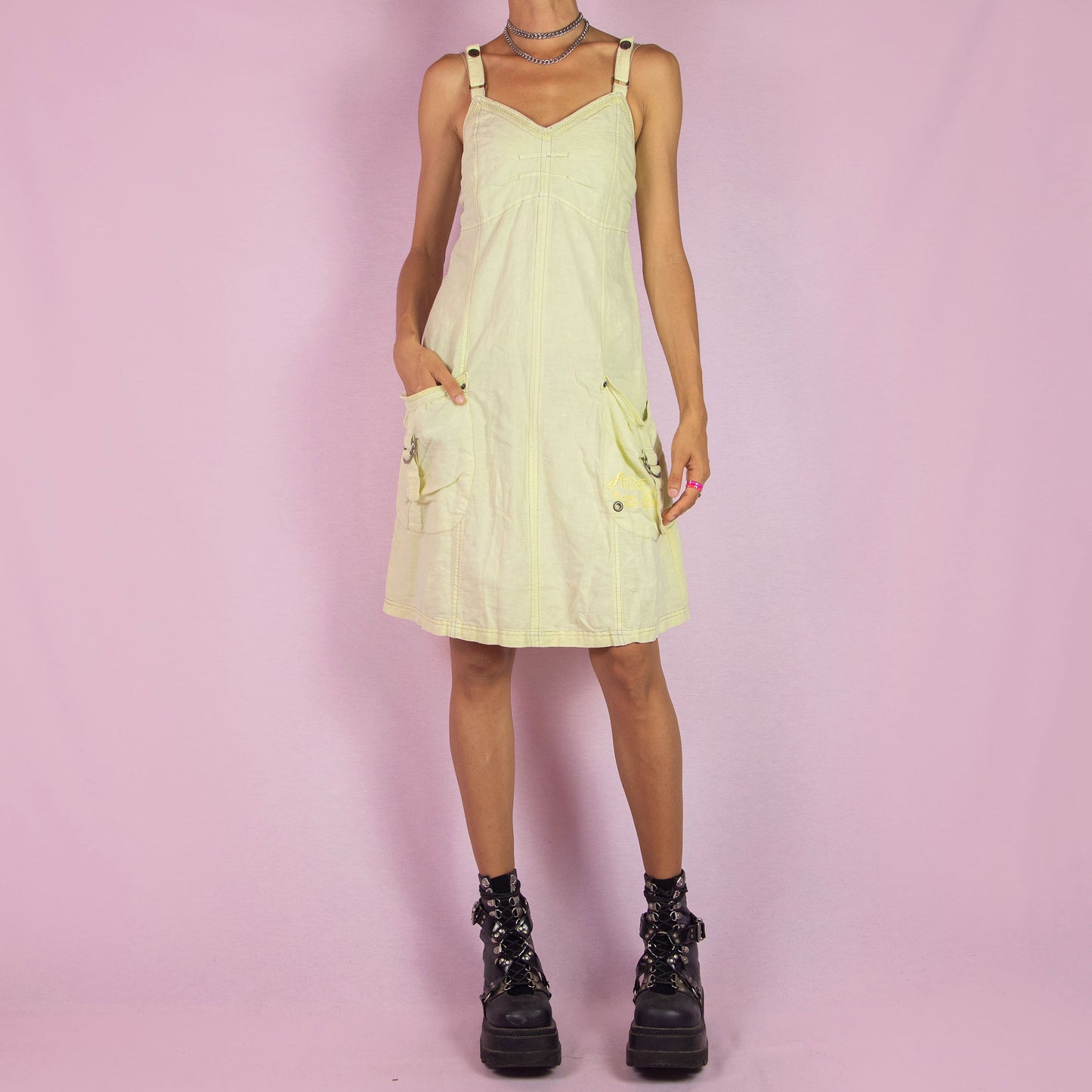 The Y2K Cotton Linen Midi Dress is a vintage 2000s piece featuring a sweetheart neckline, adjustable straps, and a back zipper closure. Made from a breathable pastel light yellow cotton-linen blend, this dress has utility-inspired details with side pockets, buckle accents, and a relaxed fit. Perfect for casual summer outings.