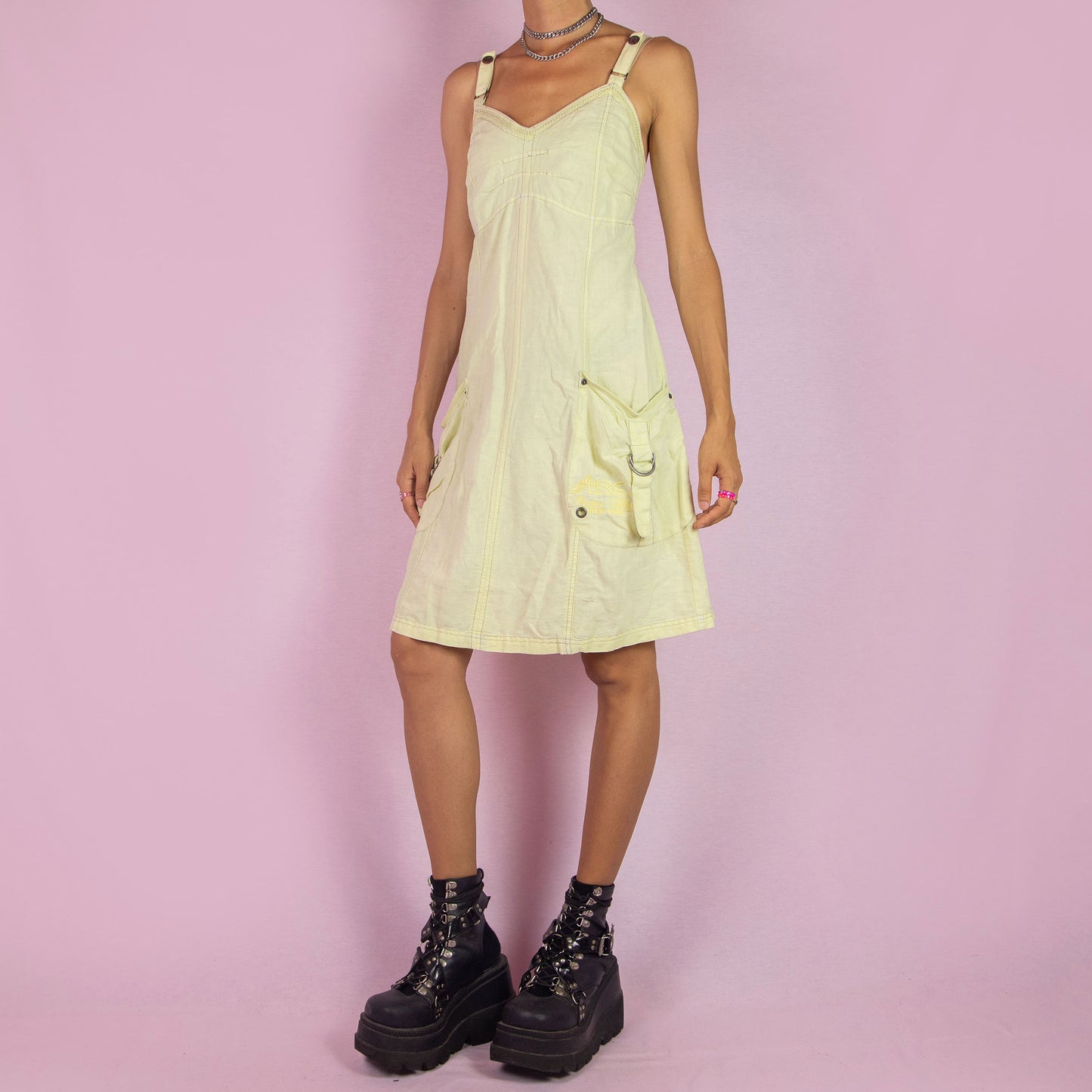 The Y2K Cotton Linen Midi Dress is a vintage 2000s piece featuring a sweetheart neckline, adjustable straps, and a back zipper closure. Made from a breathable pastel light yellow cotton-linen blend, this dress has utility-inspired details with side pockets, buckle accents, and a relaxed fit. Perfect for casual summer outings.