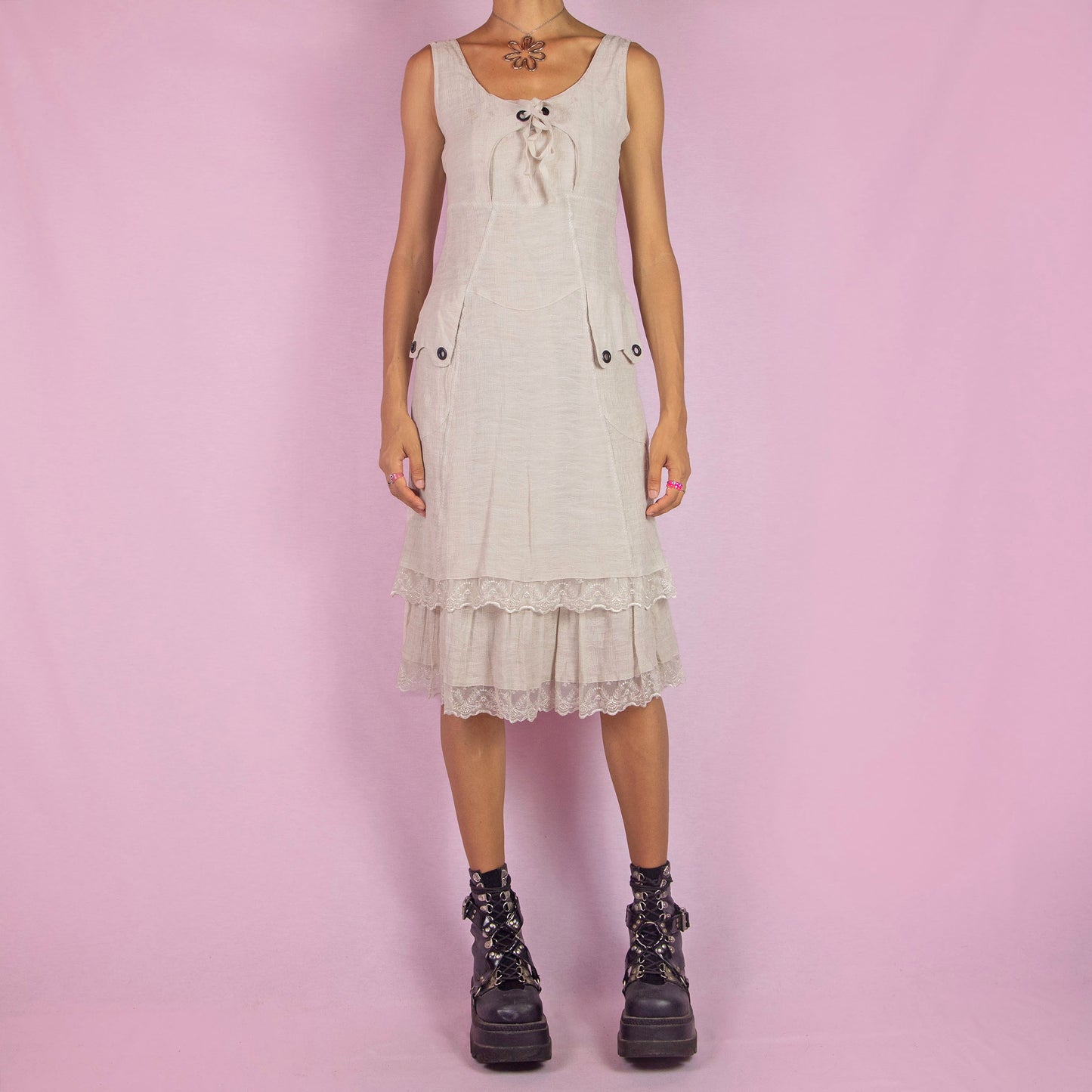 The Y2K Beige Sleeveless Midi Dress is a vintage 2000s piece featuring a lace-up front detail and a side zipper closure. Made from a textured cotton blend, this dress offers a flattering silhouette with pockets, and a charming tiered lace hem. Perfect for casual summer outings or an elegant boho-inspired look.