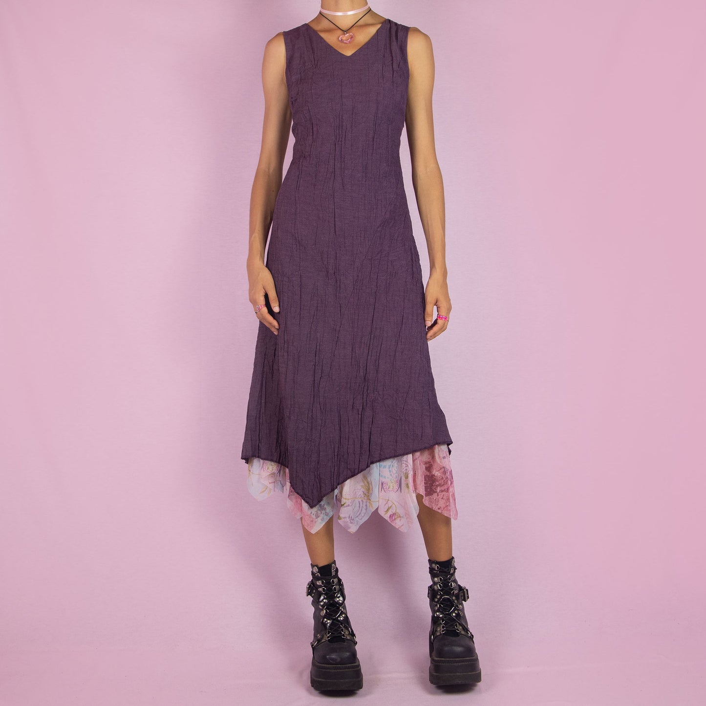 The Y2K Purple Sleeveless Midi Dress is a vintage 2000s piece featuring a crinkled, textured fabric, a V-neckline, and a side zipper closure. The dress also has a layered asymmetric hemline with an abstract floral print mesh sheer underlayer peeking out. Perfect for summer outings and elegant parties.