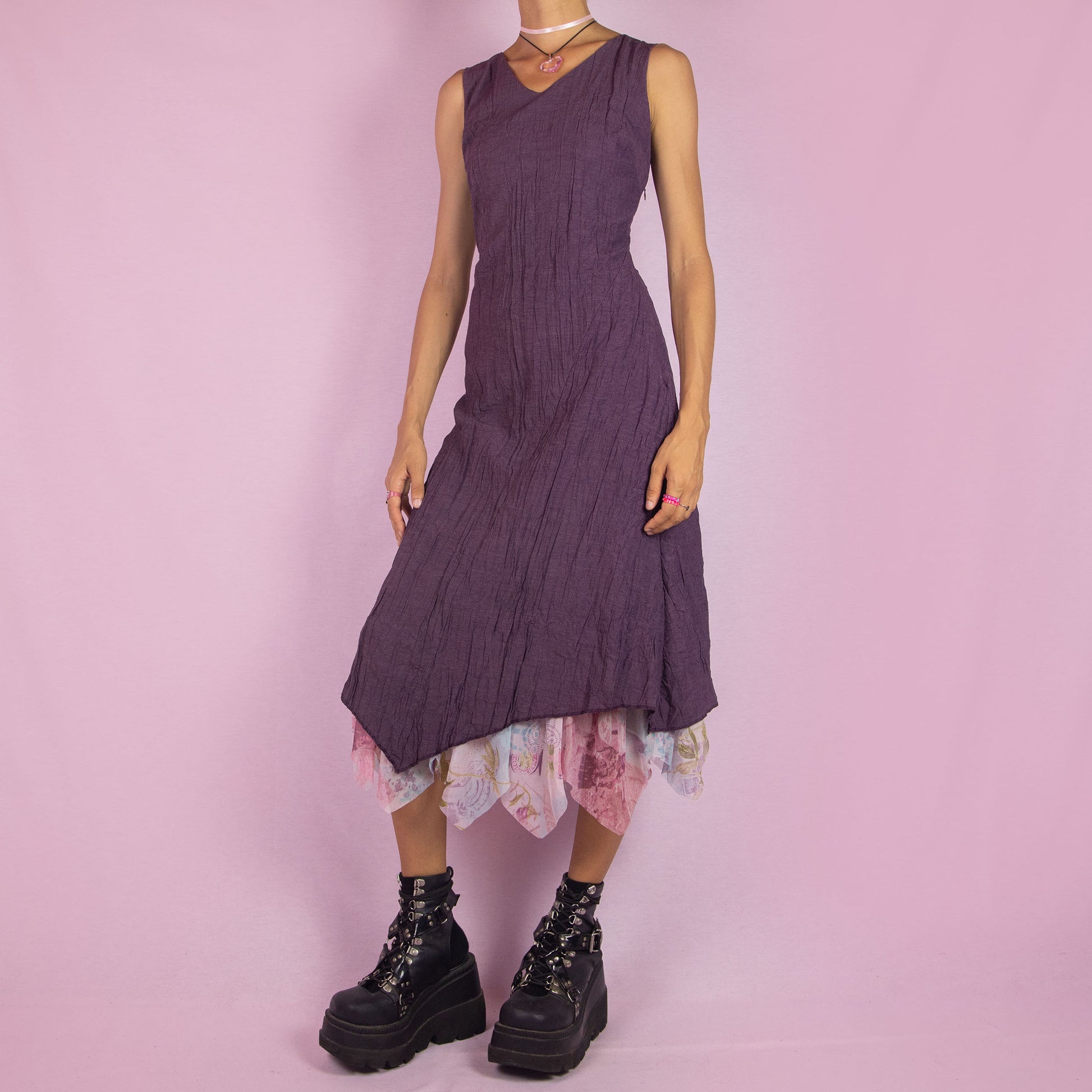 The Y2K Purple Sleeveless Midi Dress is a vintage 2000s piece featuring a crinkled, textured fabric, a V-neckline, and a side zipper closure. The dress also has a layered asymmetric hemline with an abstract floral print mesh sheer underlayer peeking out. Perfect for summer outings and elegant parties.