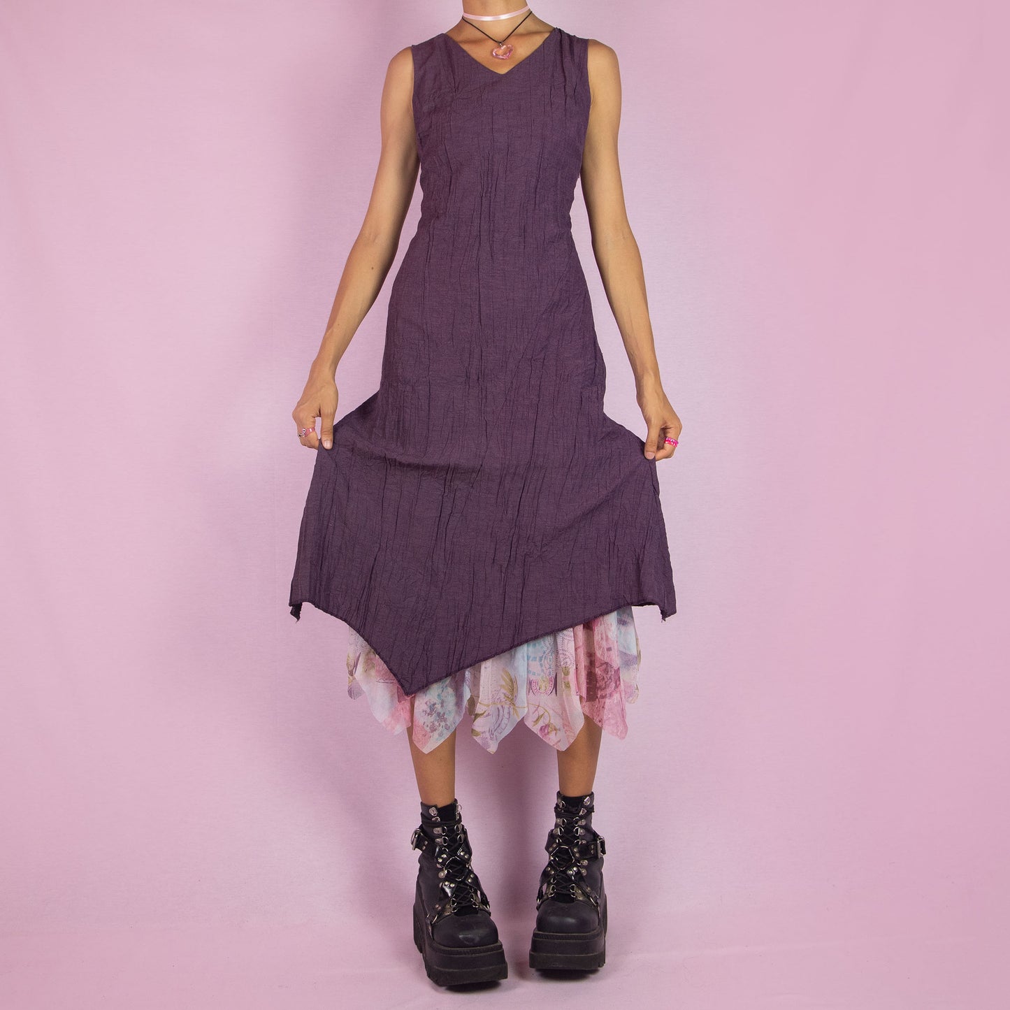 The Y2K Purple Sleeveless Midi Dress is a vintage 2000s piece featuring a crinkled, textured fabric, a V-neckline, and a side zipper closure. The dress also has a layered asymmetric hemline with an abstract floral print mesh sheer underlayer peeking out. Perfect for summer outings and elegant parties.