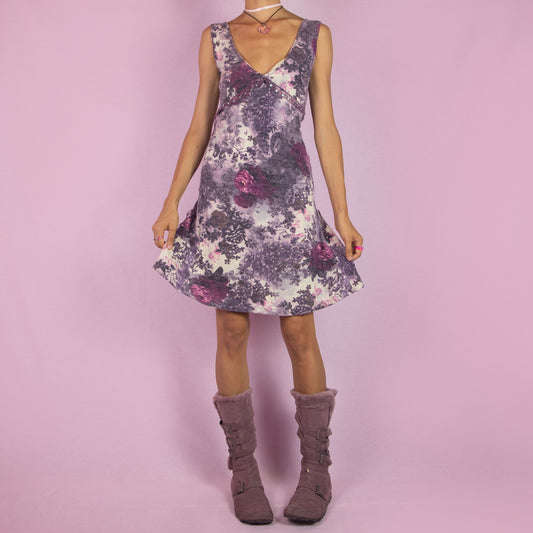 The Y2K Sleeveless Knit Midi Dress is a vintage 2000s piece featuring a stretchy fabric and a deep V-neckline. With a floral knit design in soft tones of purple and pink, this dress has a flattering A-line silhouette and subtle embellishments along the bust. Perfect for cozy casual wear or a chic day out.