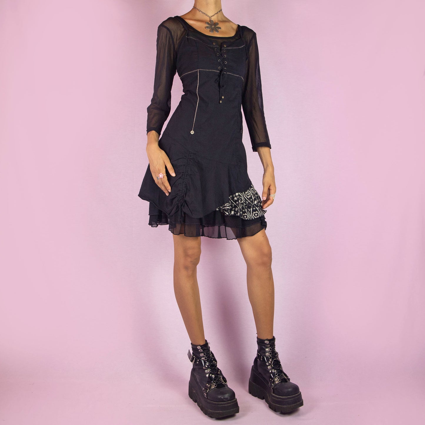 The Y2K Black Asymmetric Mesh Dress is a vintage 2000s mini dress featuring a scoop neckline, three-quarter sheer mesh sleeves, and a stretchy fabric. It has a lace-up bodice, side zipper closure, and an asymmetric hemline with gathered details and a printed panel. The layered mesh underlay gives it a whimsical touch, making it perfect for parties and night events.