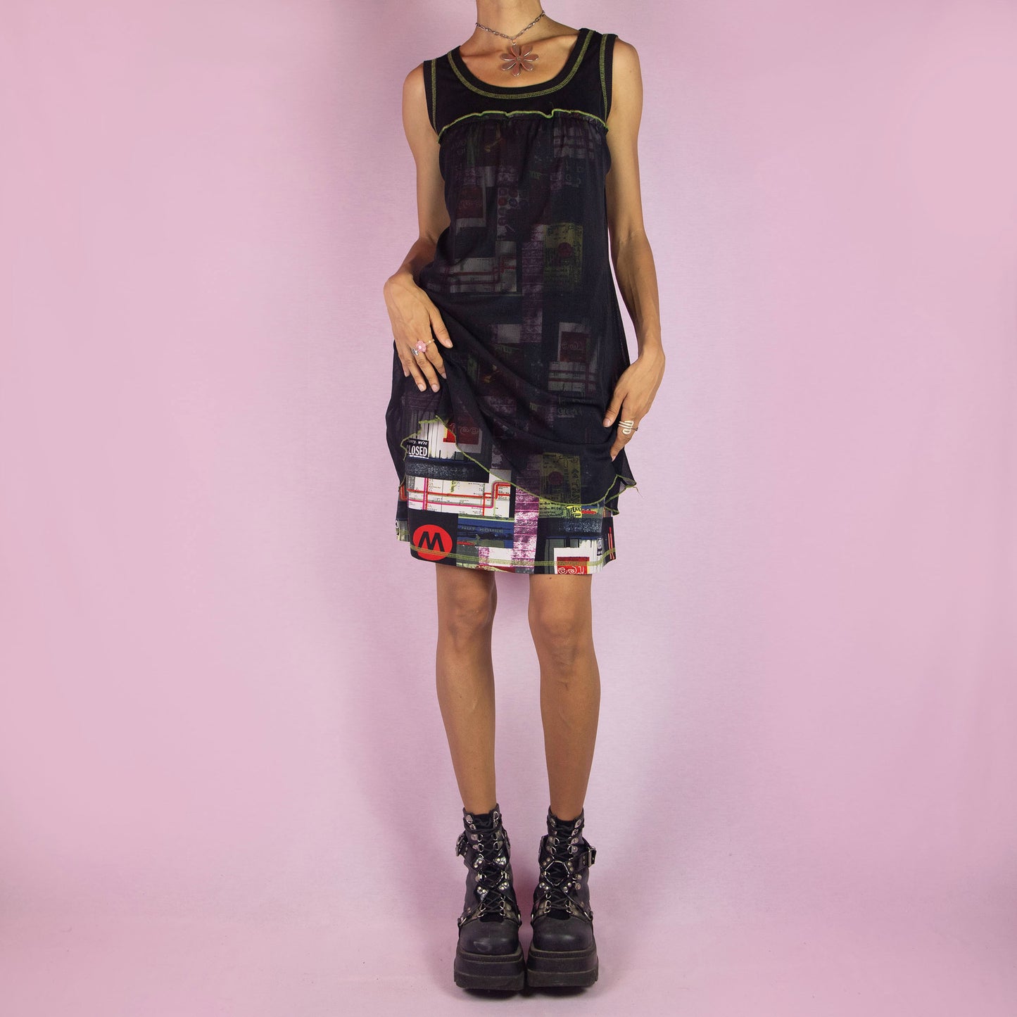 The Y2K Black Sleeveless Mesh Dress is a vintage 2000s mini dress featuring a scoop neckline, relaxed fit, and lightweight mesh fabric. The dress is adorned with abstract prints and neon green stitching along the neckline and hem. Its layered design and playful details make it perfect for casual summer outings.