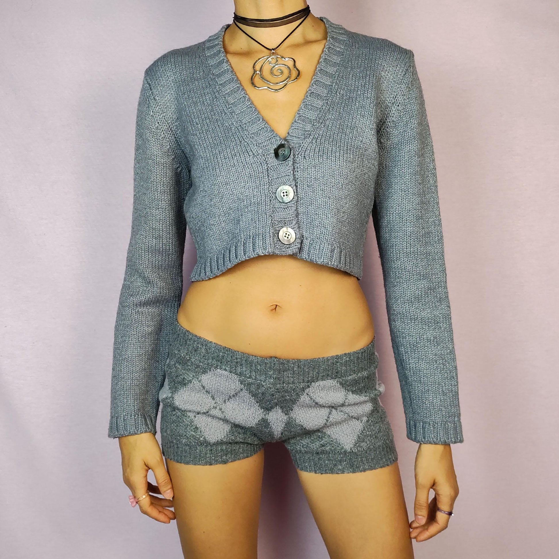 The Y2K Gray Cropped Cardigan is a vintage 2000s sweater featuring a classic V-neck design with a button-front closure, long sleeves, and ribbed detailing on the hem and cuffs. Crafted from a merino wool and acrylic blend