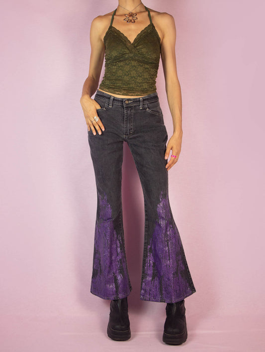 The Y2K Gray Flare Jeans are a vintage 2000s mid-rise pants featuring stretchy gray denim with purple glitter paint splatter detailing on the flared legs, front pockets, and a zipper closure. Perfect for festival looks or casual outfits. Made in UK.