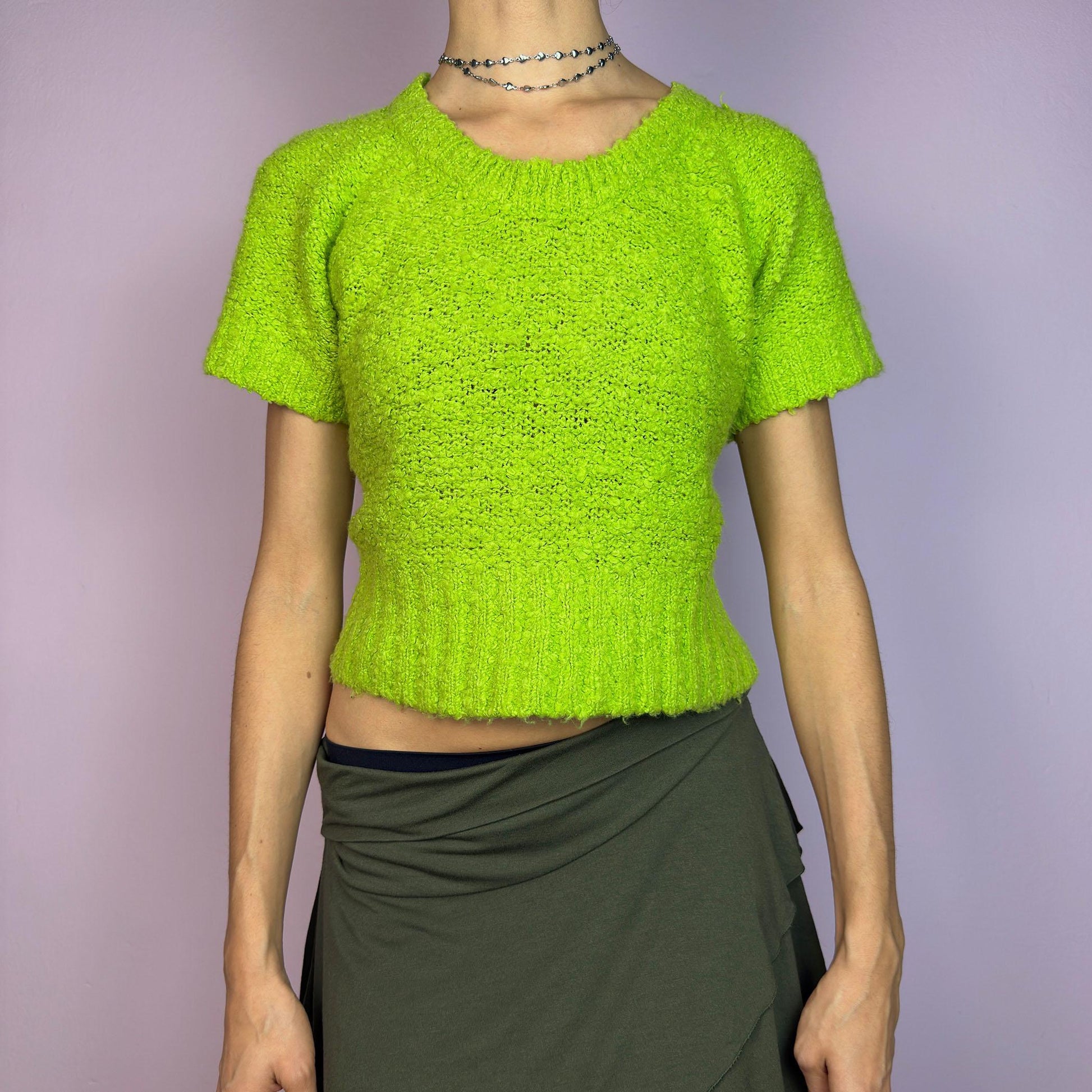 The Y2K Green Knitted Top is a vibrant vintage 2000s piece featuring a lime-green hue. Designed with a cropped silhouette, short sleeves, and a stretchy ribbed hem, this knit top adds a playful touch to casual outfits. adult world shop