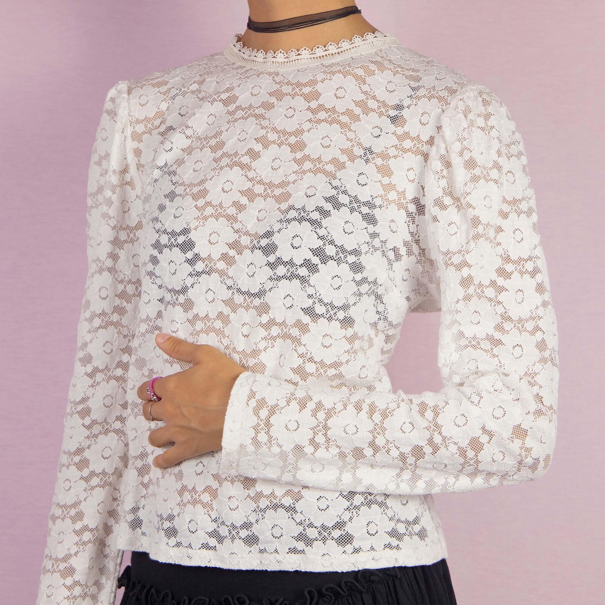 The Y2K White Lace Blouse is a vintage 2000s elegant top featuring intricate floral lace patterns in a semi-sheer design. It showcases puff sleeves and a high neckline adorned with delicate lace trim. The blouse is finished with a back button