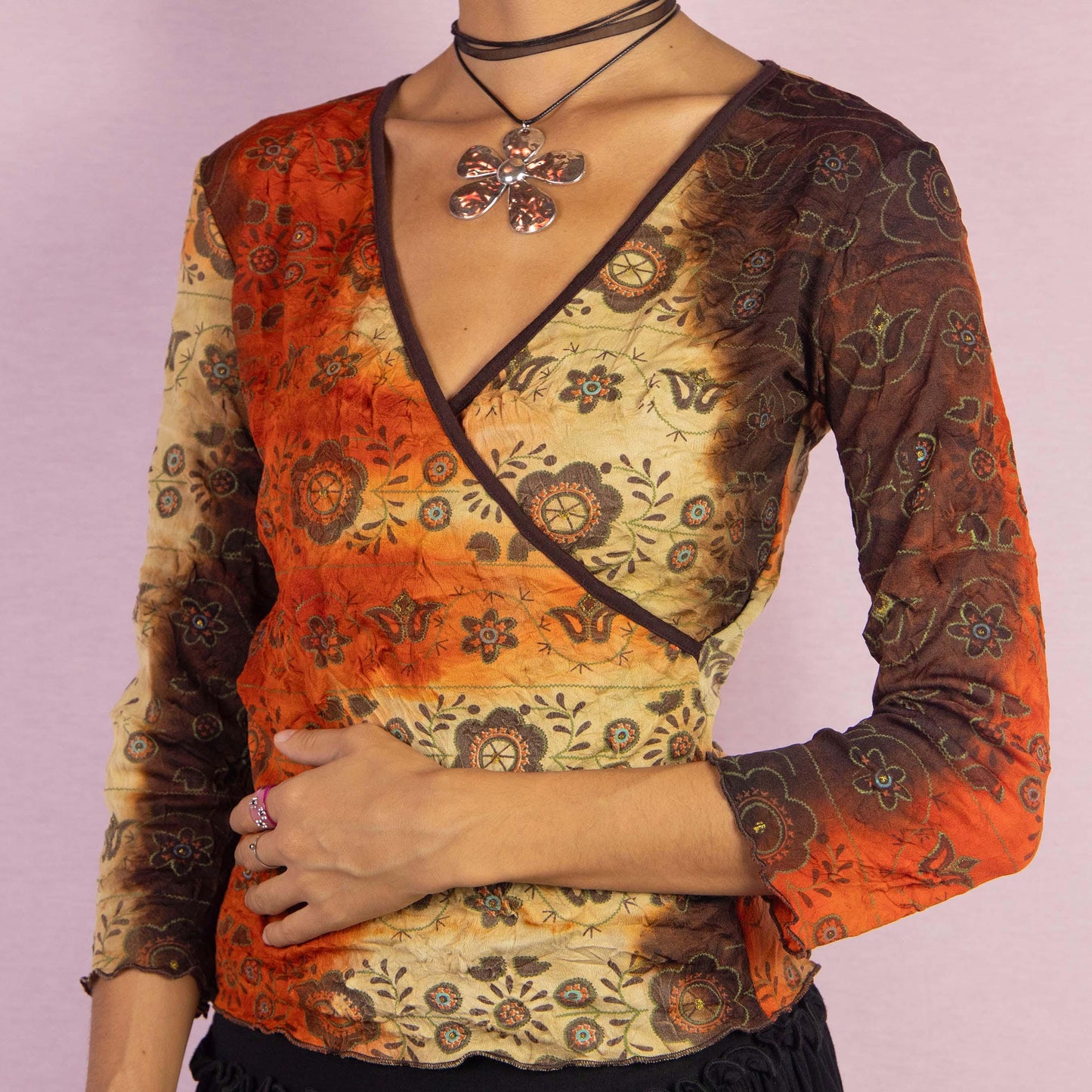 The Y2K Tie Dye Wrap Top is a vintage 2000s shirt featuring a tie-dye-inspired gradient in earthy orange and brown hues, complemented by mandala-inspired patterns. This top showcases a flattering wrap-style silhouette with a deep V-neckline