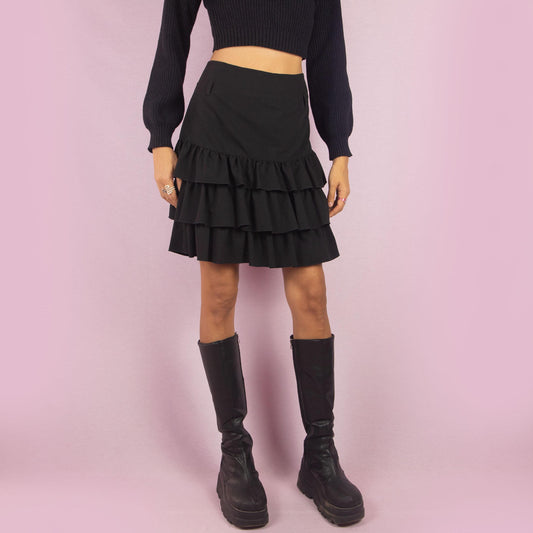 The Y2K Ruffle Black Mini Skirt is a vintage 2000s piece featuring playful tiered ruffles and a side zipper closure. Its mini length and flattering fit make it perfect for casual outings and evening events.