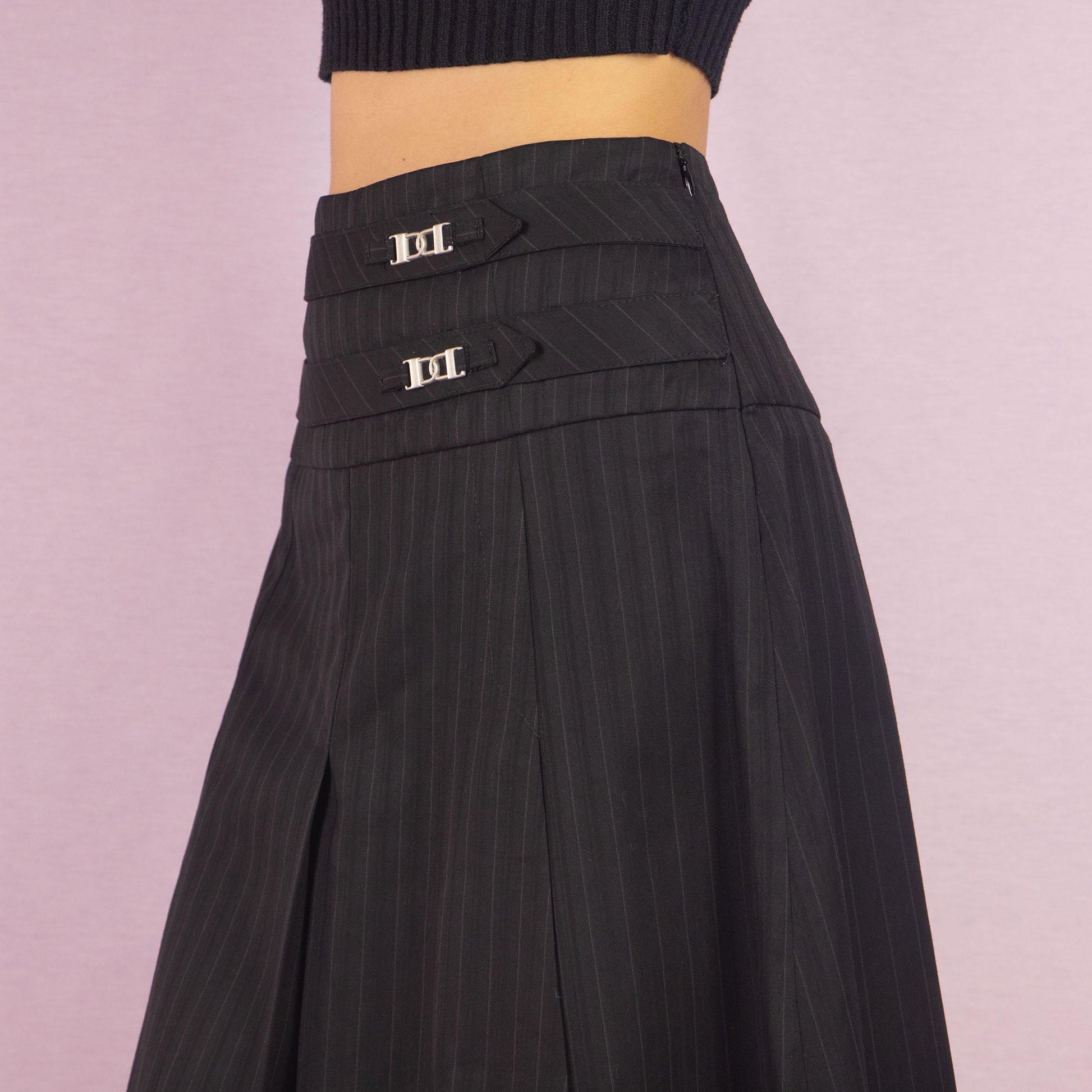 The Y2K Pinstripe Pleated Mini Skirt is a vintage 2000s piece featuring a classic pinstripe pattern with pleated detailing in black. Designed with a mid-rise fit, mini length, and side zipper closure, it’s perfect for office-to-evening transitions