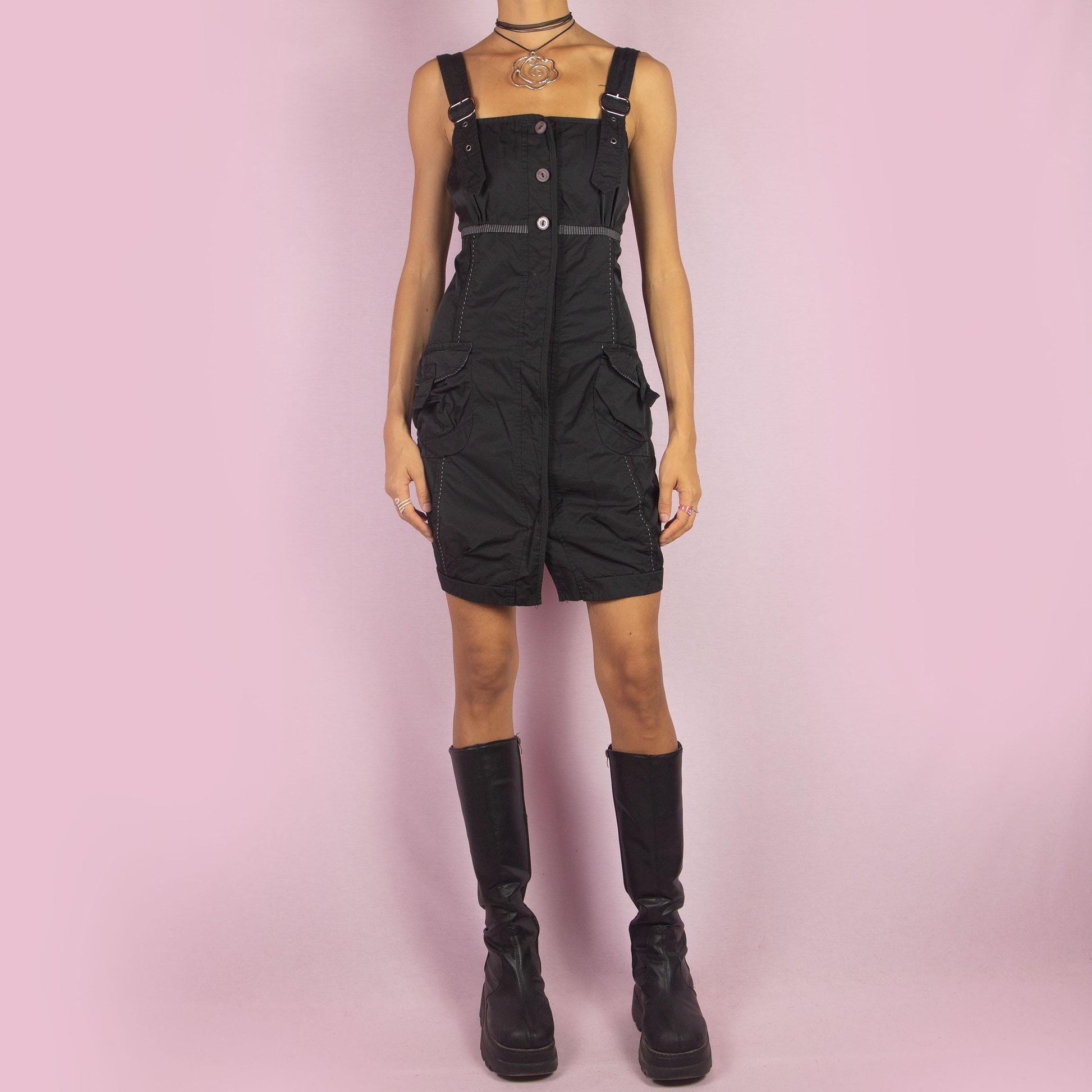 The Y2K Buckle Strap Black Mini Dress is a vintage 2000s piece featuring adjustable buckle straps, a button-down front, and utility-style pockets. Designed with contrast stitching and a structured silhouette, this mini dress is perfect for daytime