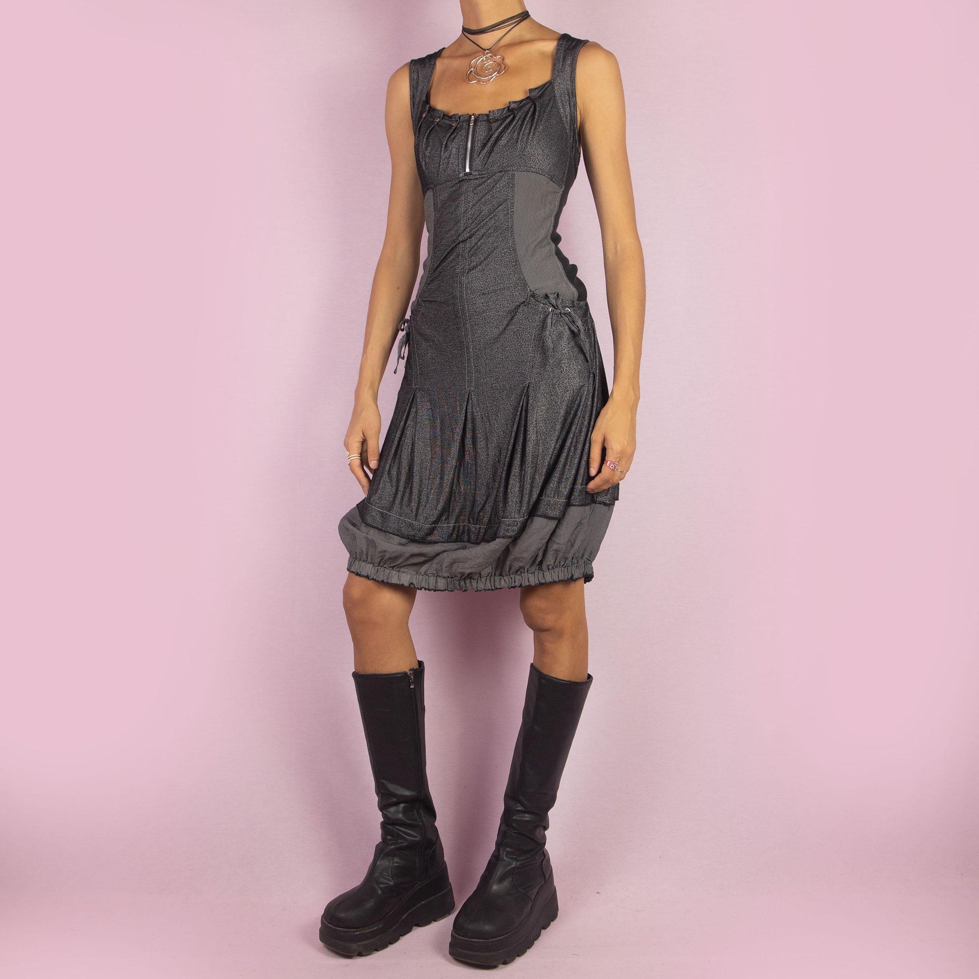 The Y2K Gray Bubble Mini Dress is a vintage 2000s piece featuring a striped, stretchy fabric with a structured bodice and a front zipper detail. The design includes pockets with drawstrings and the bubble hemline adds volume and playfulness.