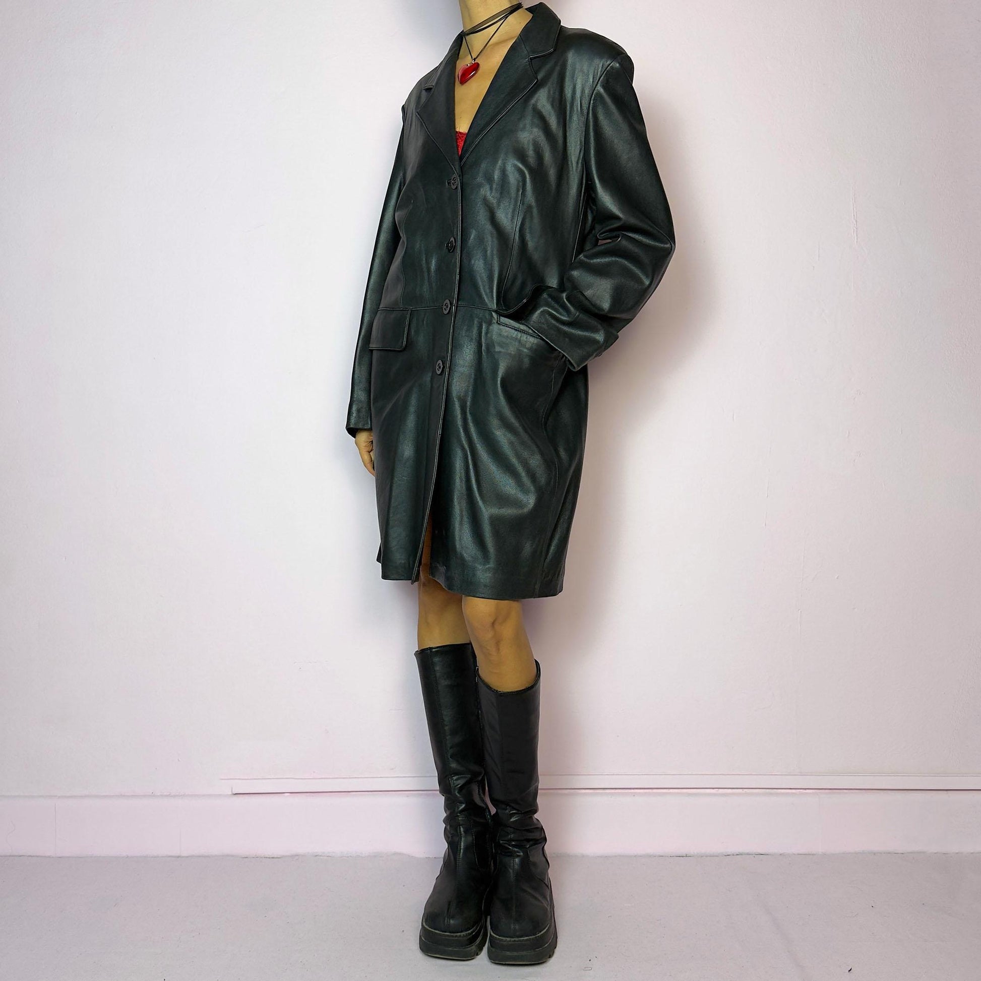 The Vintage 90s Black Leather Coat features a timeless design crafted from genuine black leather, with a button-front closure and a tailored silhouette. Complete with pockets, this versatile coat is ideal for both casual and formal occasions.