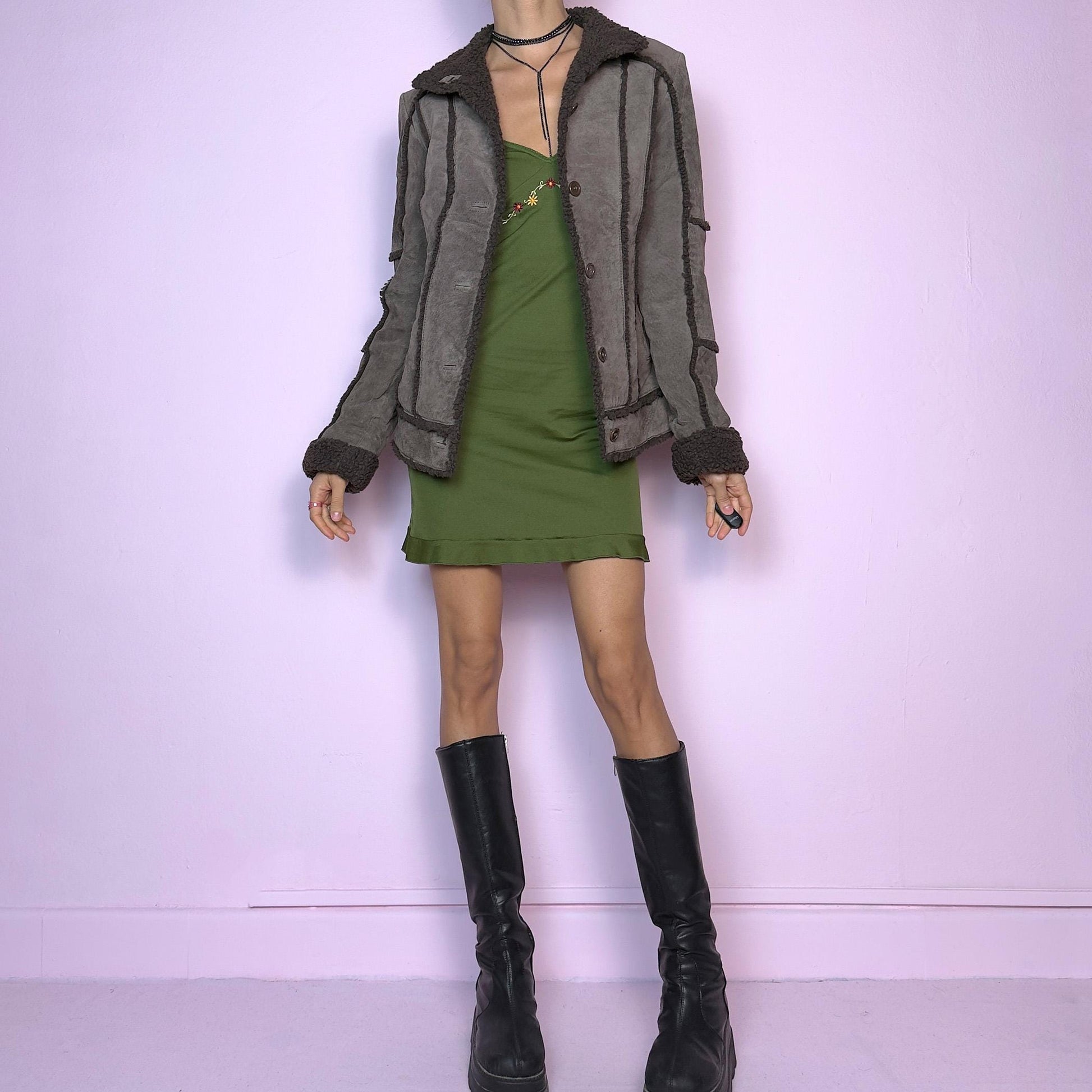 The Vintage 90s Split Suede Leather Jacket features a dark khaki brownish hue, showcasing split suede material. Soft faux shearling details on the collar, cuffs, and trim add warmth and a cozy aesthetic. Its button-front closure and structured fit