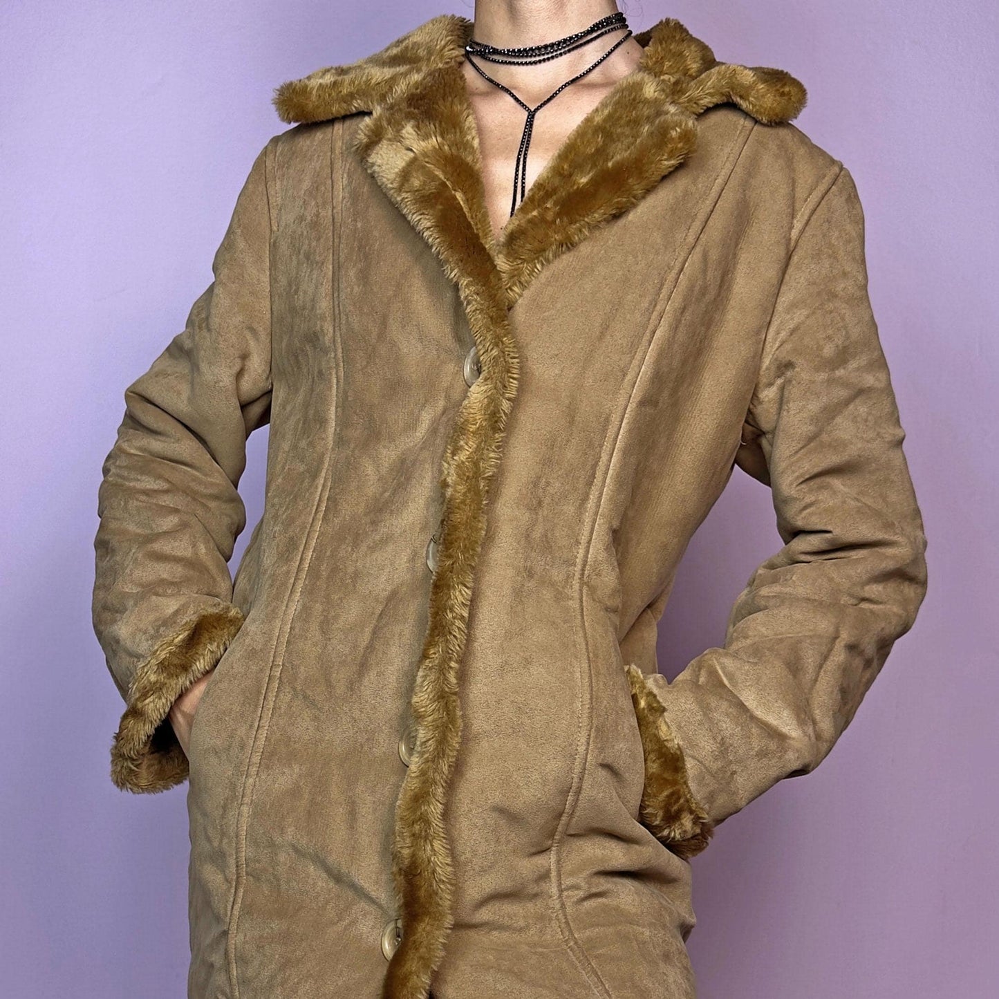 The Y2K Faux Suede Maxi Coat is a vintage 2000s cozy piece featuring a classic camel-tone faux suede exterior accented with plush faux fur trim along the collar, cuffs, and hem. This longline coat includes button-front closures and a tailored fit