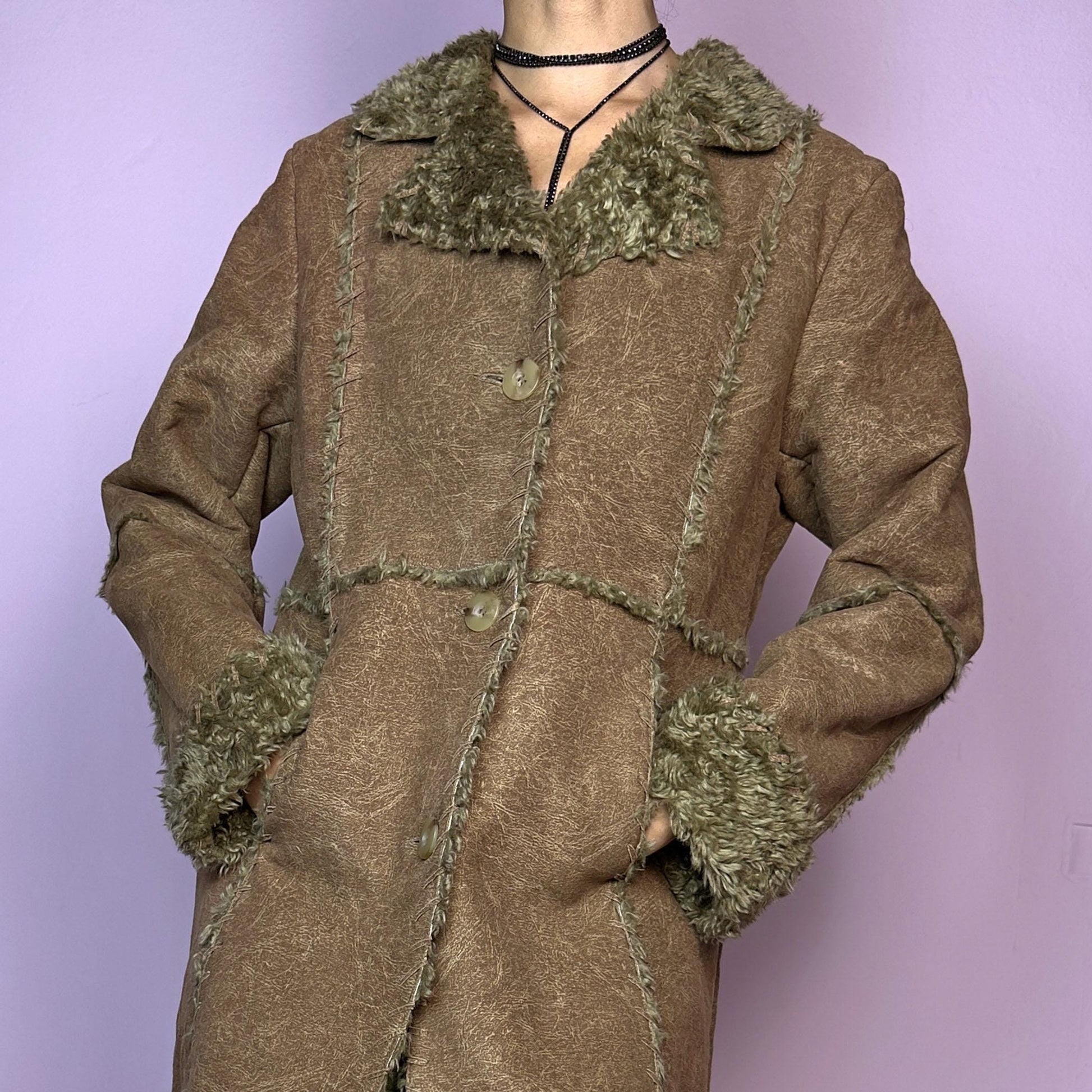 The Y2K Faux Fur Suede Long Coat is a vintage 2000s cozy piece featuring a soft brown faux suede exterior and faux shearling trim along the collar, cuffs, and seams. Its structured silhouette features button-front closure and pockets