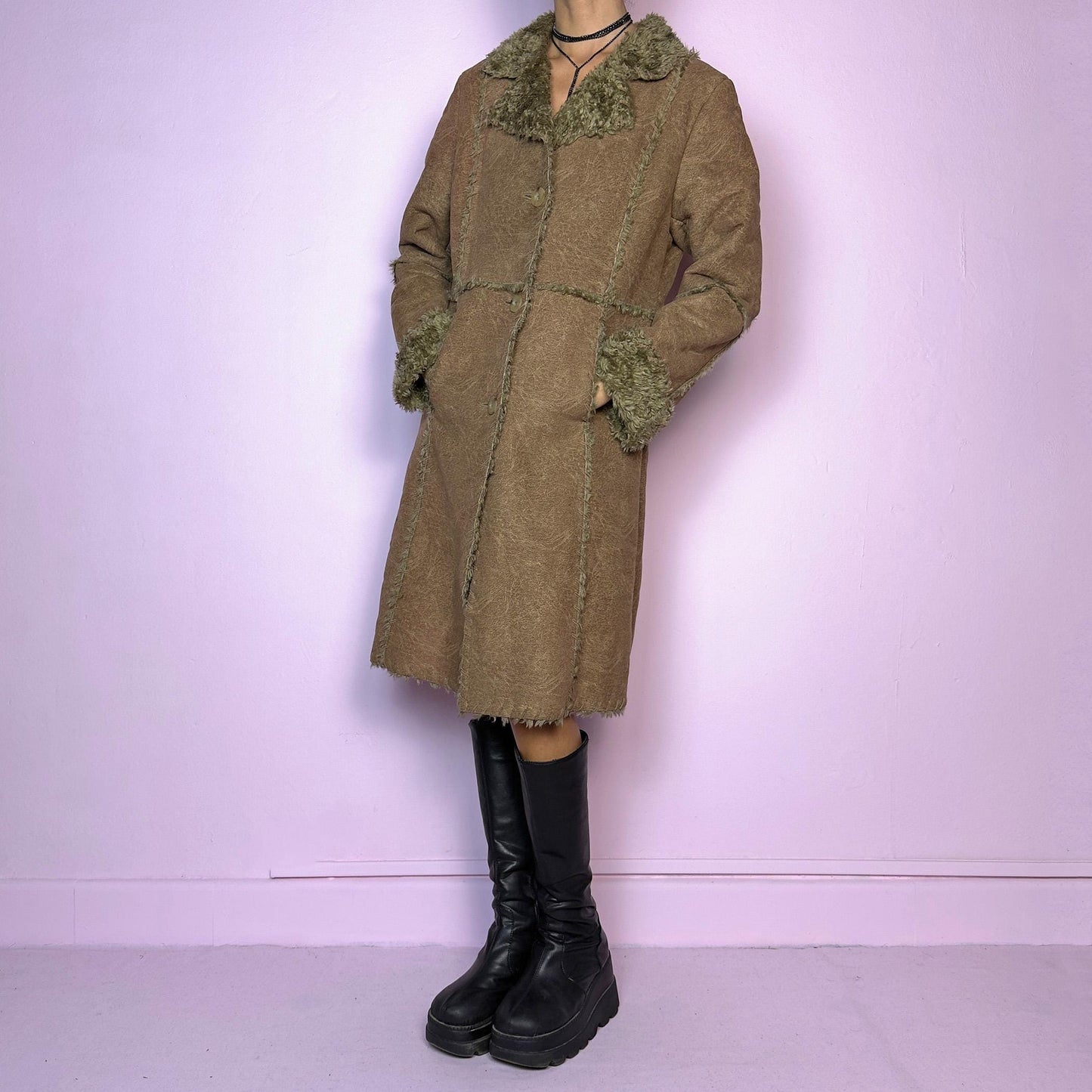 The Y2K Faux Fur Suede Long Coat is a vintage 2000s cozy piece featuring a soft brown faux suede exterior and faux shearling trim along the collar, cuffs, and seams. Its structured silhouette features button-front closure and pockets