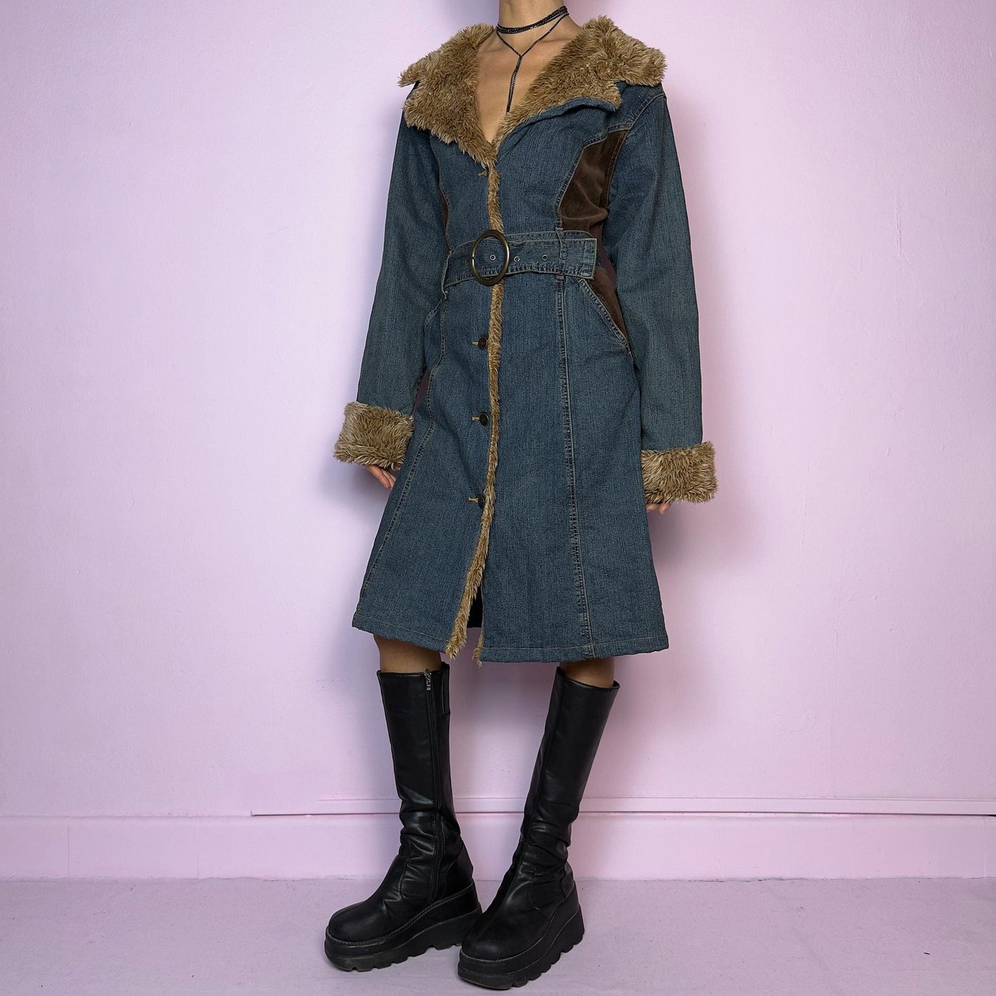 The Y2K Faux Fur Denim Coat is a vintage 2000s piece blending blue denim with cozy brown faux fur trim along the collar, front, cuffs, and hem. It also includes a matching belt with a circular buckle that creates a flattering silhouette