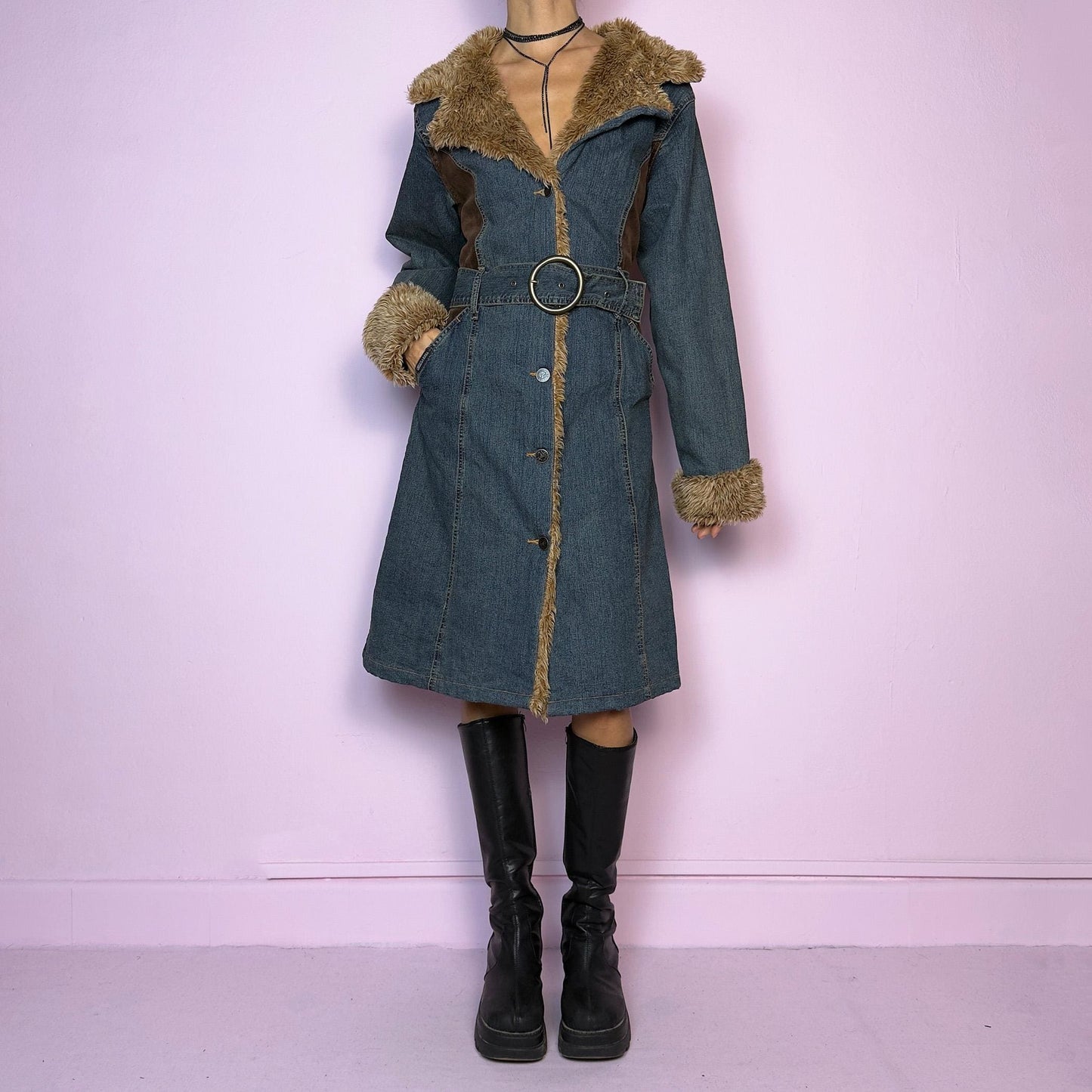 The Y2K Faux Fur Denim Coat is a vintage 2000s piece blending blue denim with cozy brown faux fur trim along the collar, front, cuffs, and hem. It also includes a matching belt with a circular buckle that creates a flattering silhouette