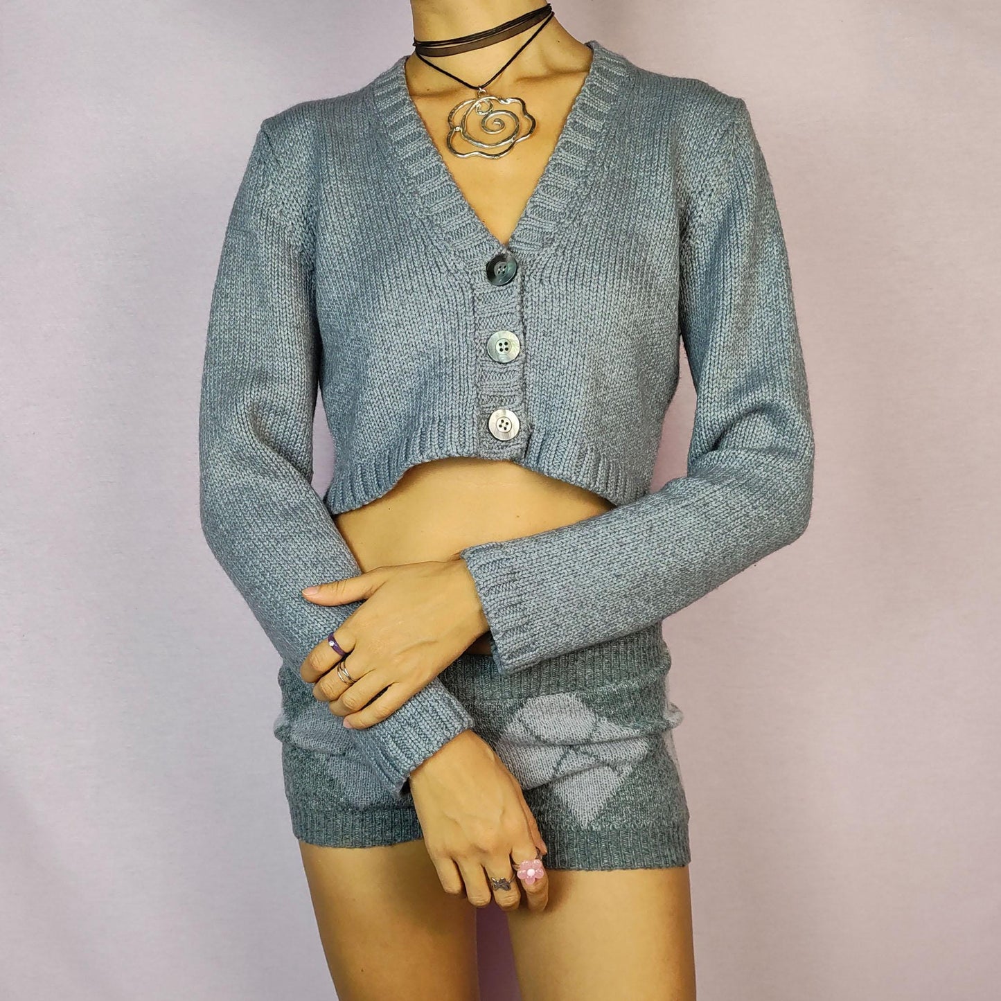 The Y2K Gray Cropped Cardigan is a vintage 2000s sweater featuring a classic V-neck design with a button-front closure, long sleeves, and ribbed detailing on the hem and cuffs. Crafted from a merino wool and acrylic blend