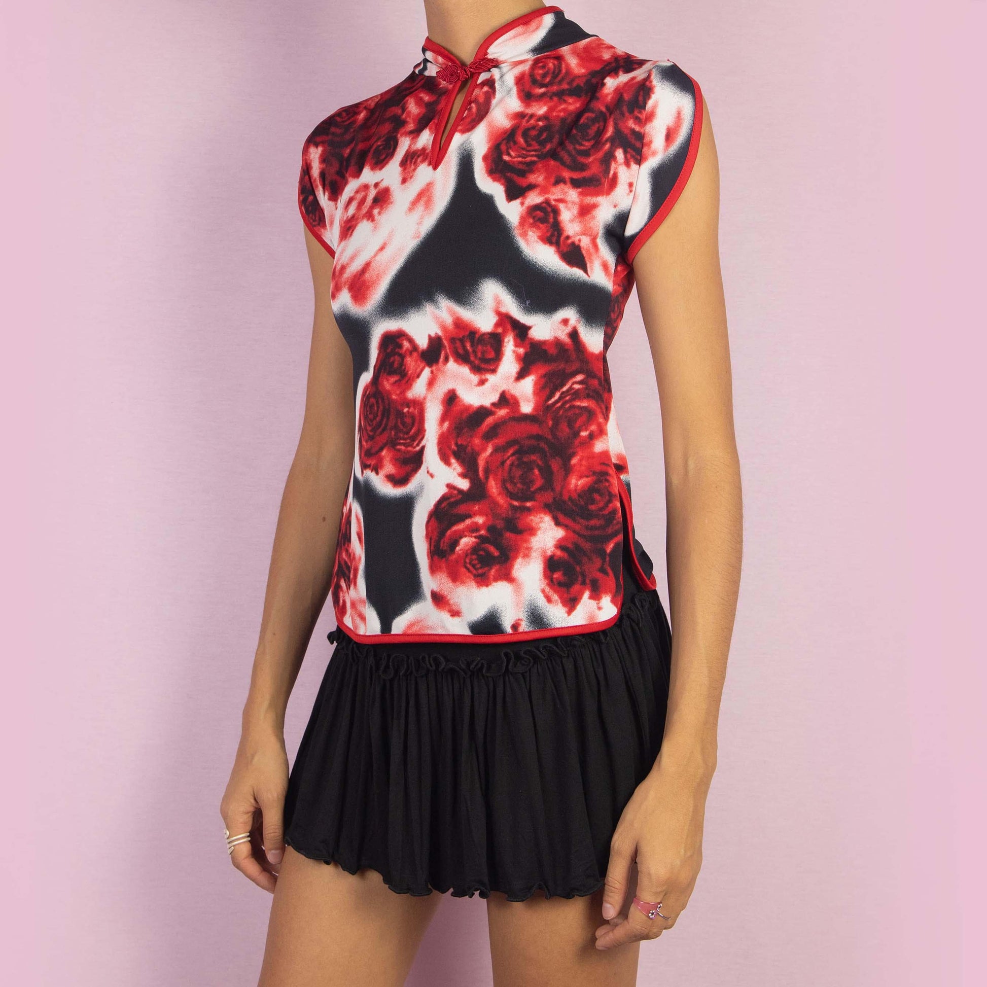 The Vintage 90s Rose Print Top is a striking piece featuring a bold red and black rose print and cap sleeves. The design is enhanced by a Qipao-inspired high collar with a decorative frog closure and a keyhole detail.