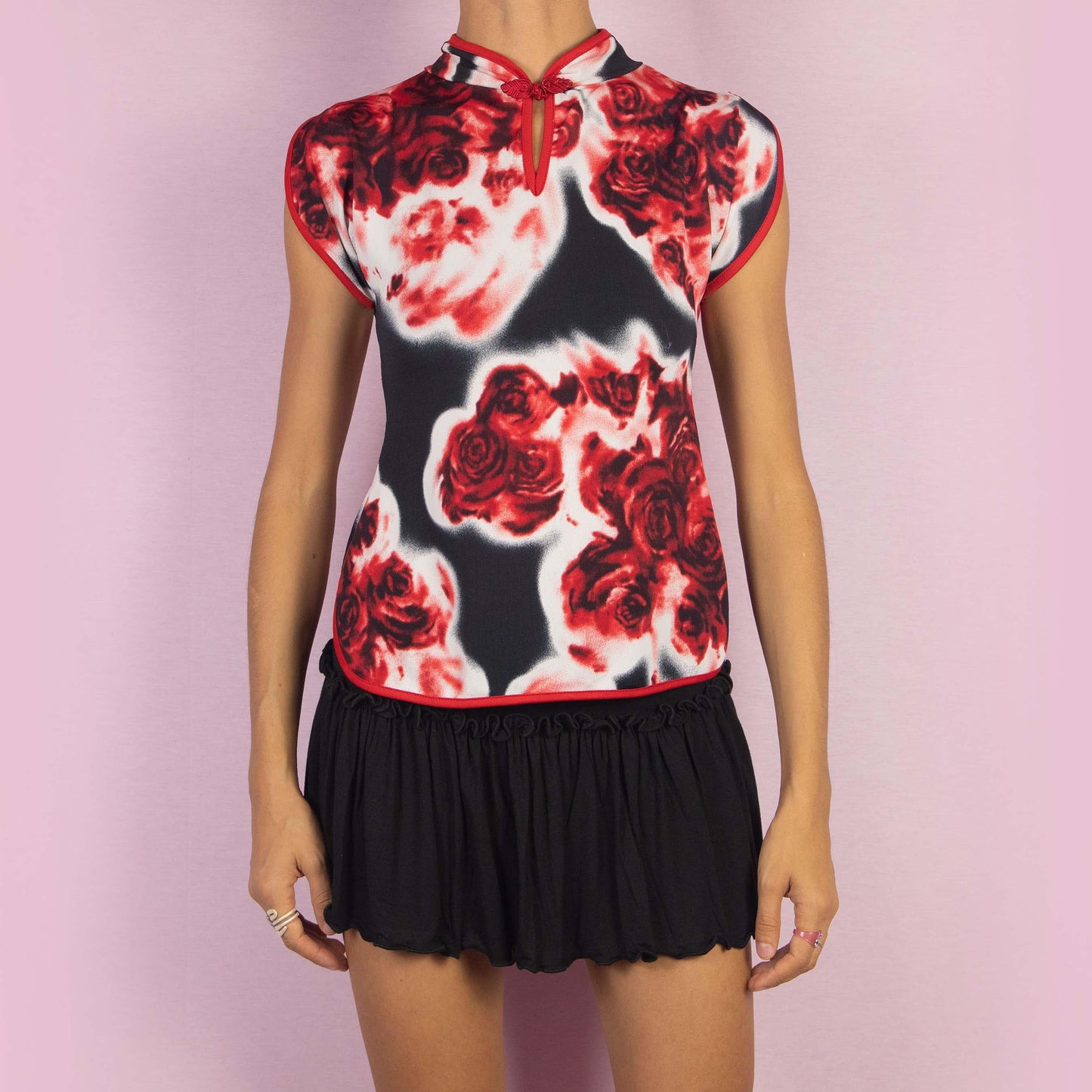 The Vintage 90s Rose Print Top is a striking piece featuring a bold red and black rose print and cap sleeves. The design is enhanced by a Qipao-inspired high collar with a decorative frog closure and a keyhole detail.