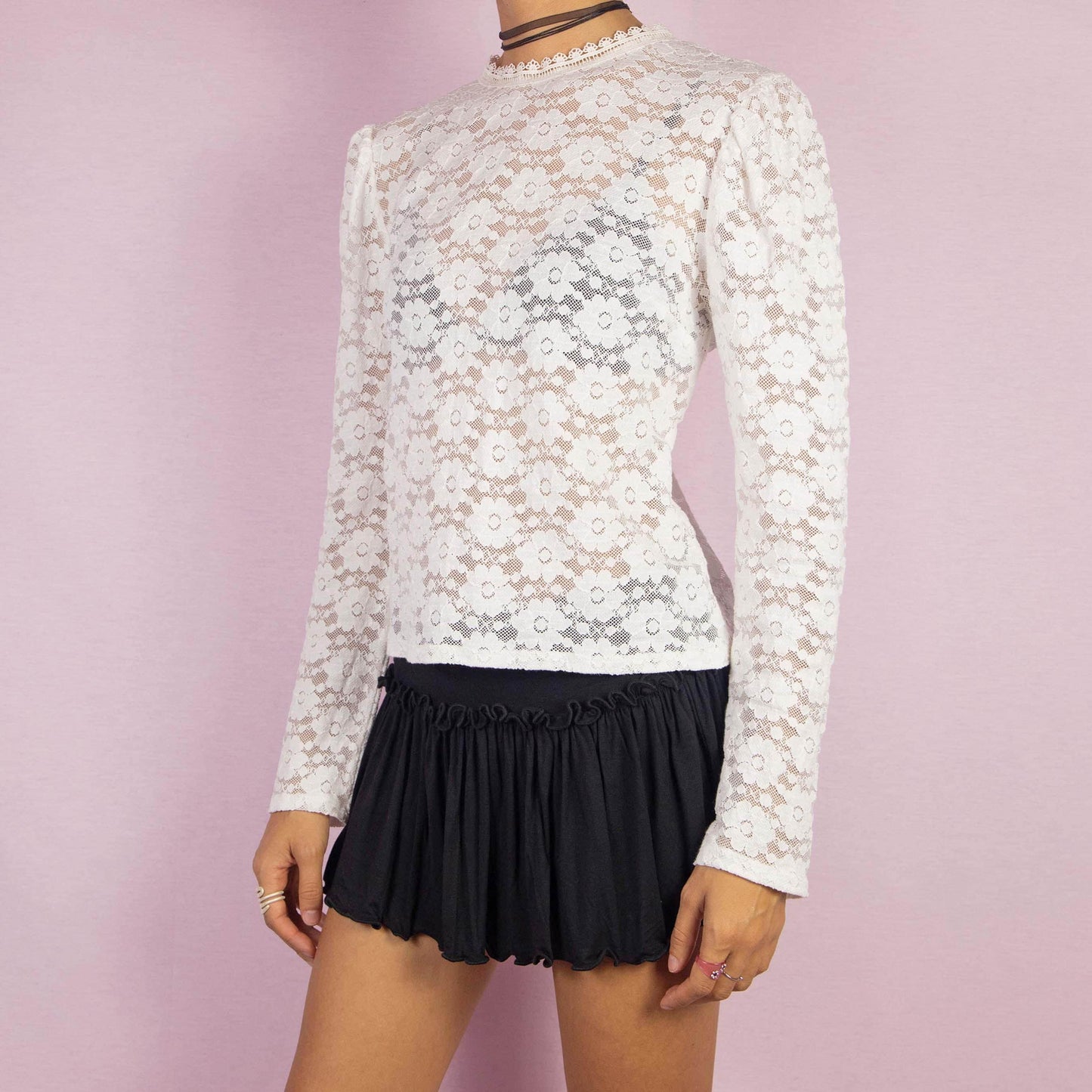 The Y2K White Lace Blouse is a vintage 2000s elegant top featuring intricate floral lace patterns in a semi-sheer design. It showcases puff sleeves and a high neckline adorned with delicate lace trim. The blouse is finished with a back button