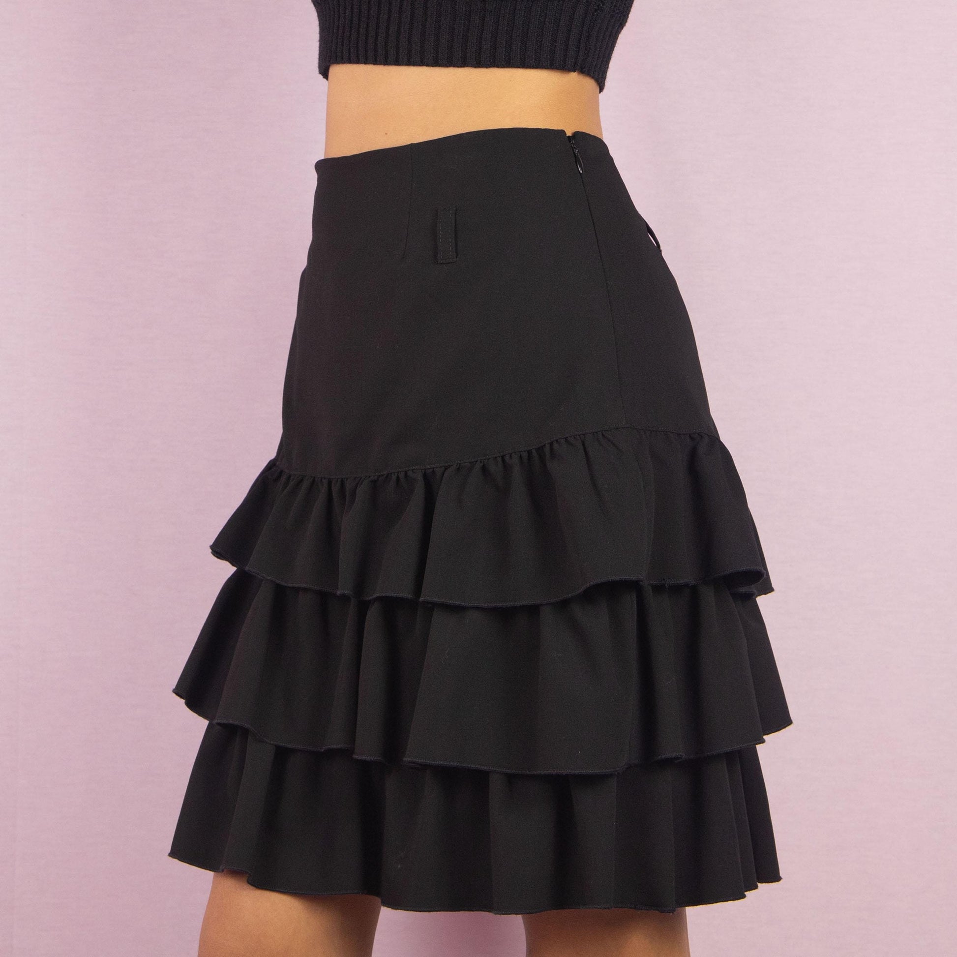 The Y2K Ruffle Black Mini Skirt is a vintage 2000s piece featuring playful tiered ruffles and a side zipper closure. Its mini length and flattering fit make it perfect for casual outings and evening events.