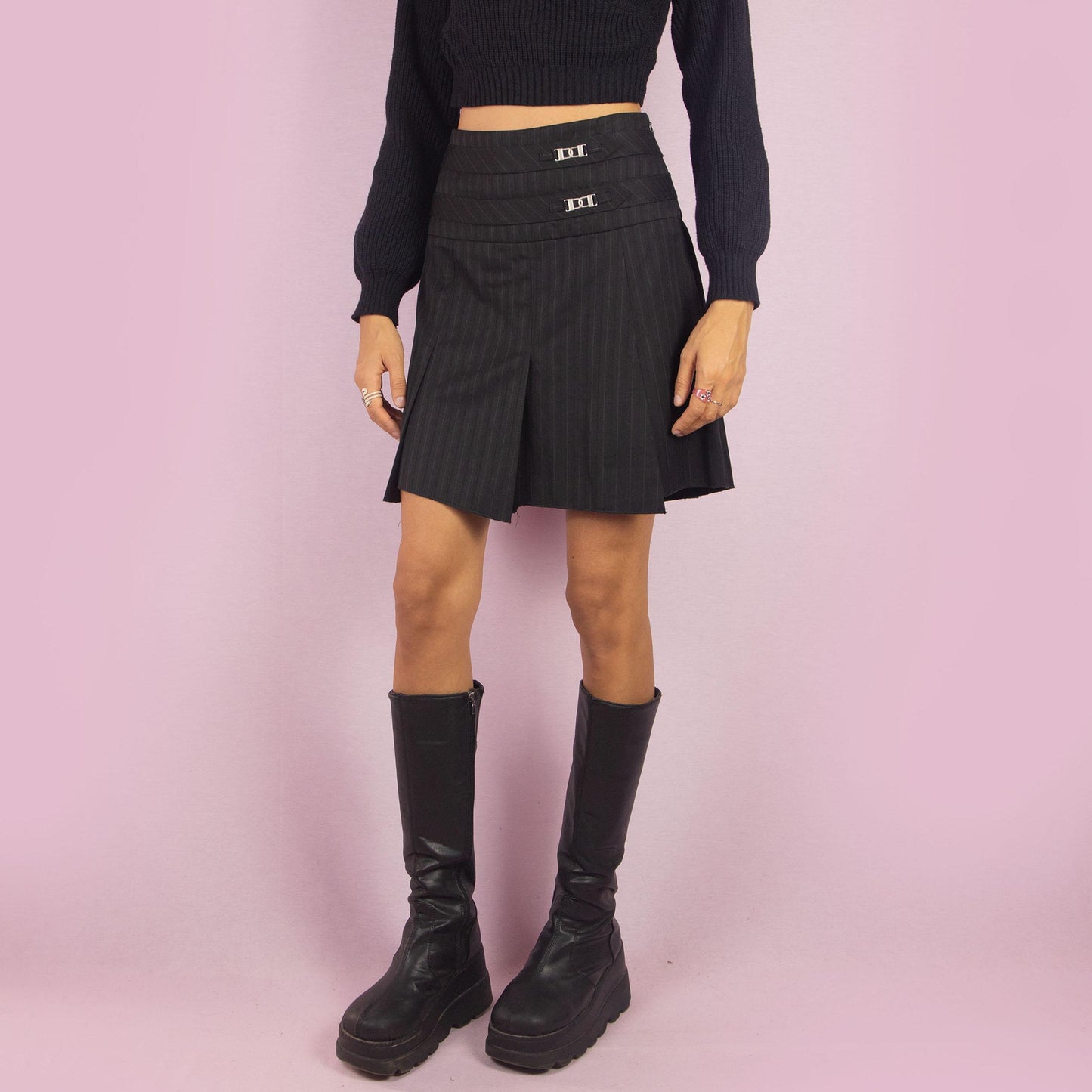 The Y2K Pinstripe Pleated Mini Skirt is a vintage 2000s piece featuring a classic pinstripe pattern with pleated detailing in black. Designed with a mid-rise fit, mini length, and side zipper closure, it’s perfect for office-to-evening transitions