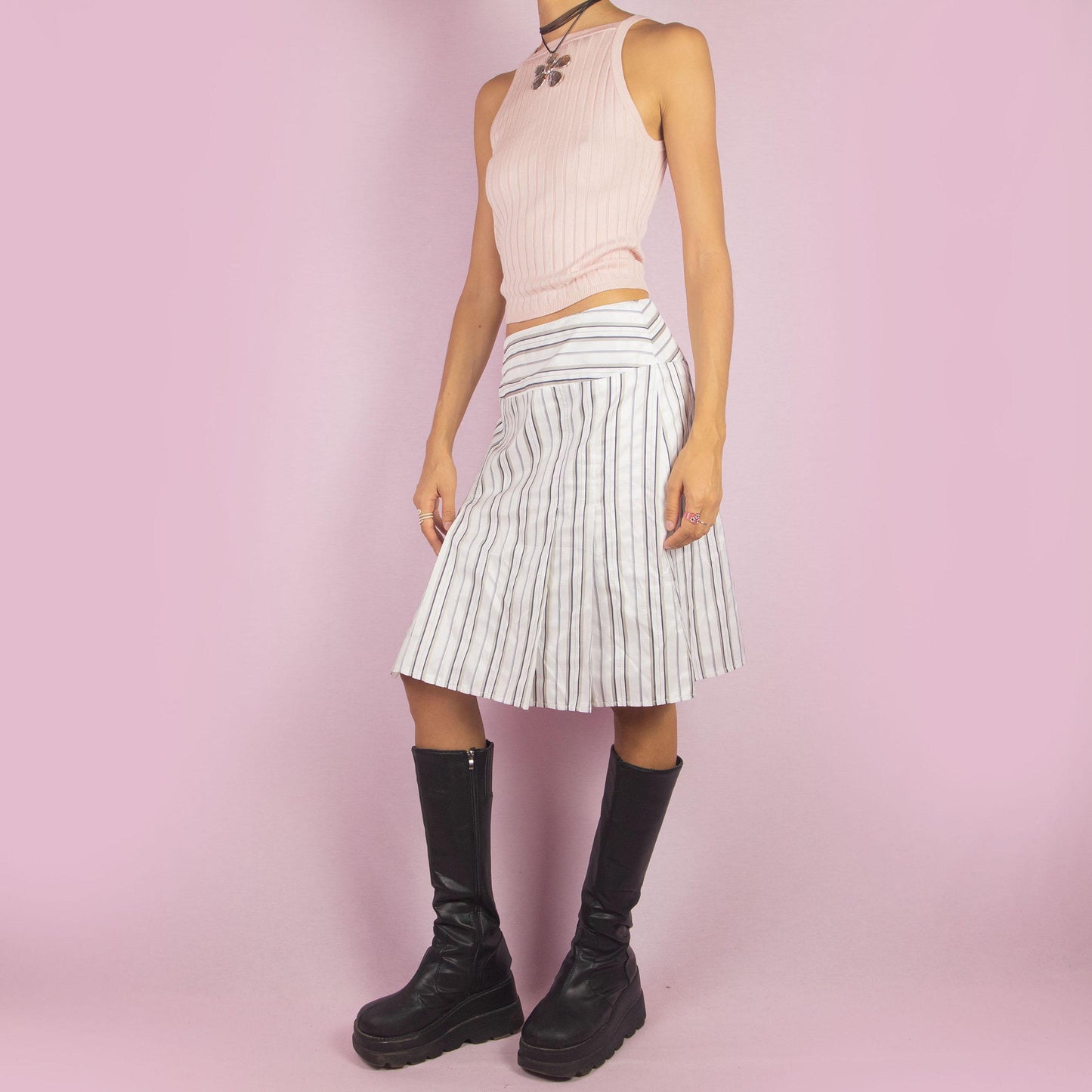 The Vintage 90s White Pinstripe Pleated Skirt features a classic pinstripe pattern with a flared silhouette, a mid-waist fit and a back zipper closure. Perfect for both office wear and casual outings.