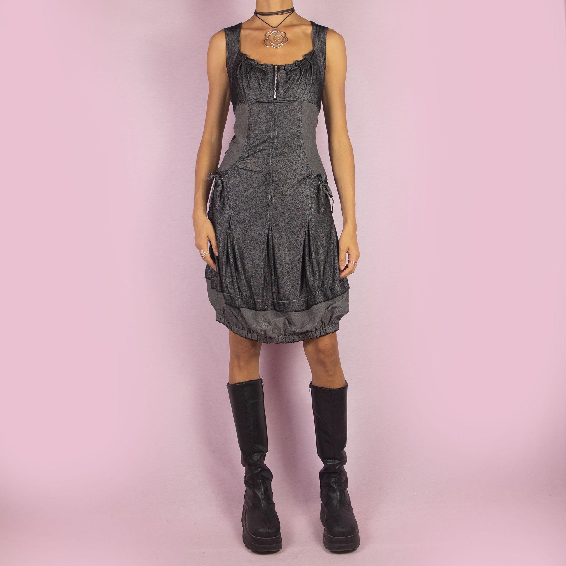 The Y2K Gray Bubble Mini Dress is a vintage 2000s piece featuring a striped, stretchy fabric with a structured bodice and a front zipper detail. The design includes pockets with drawstrings and the bubble hemline adds volume and playfulness.