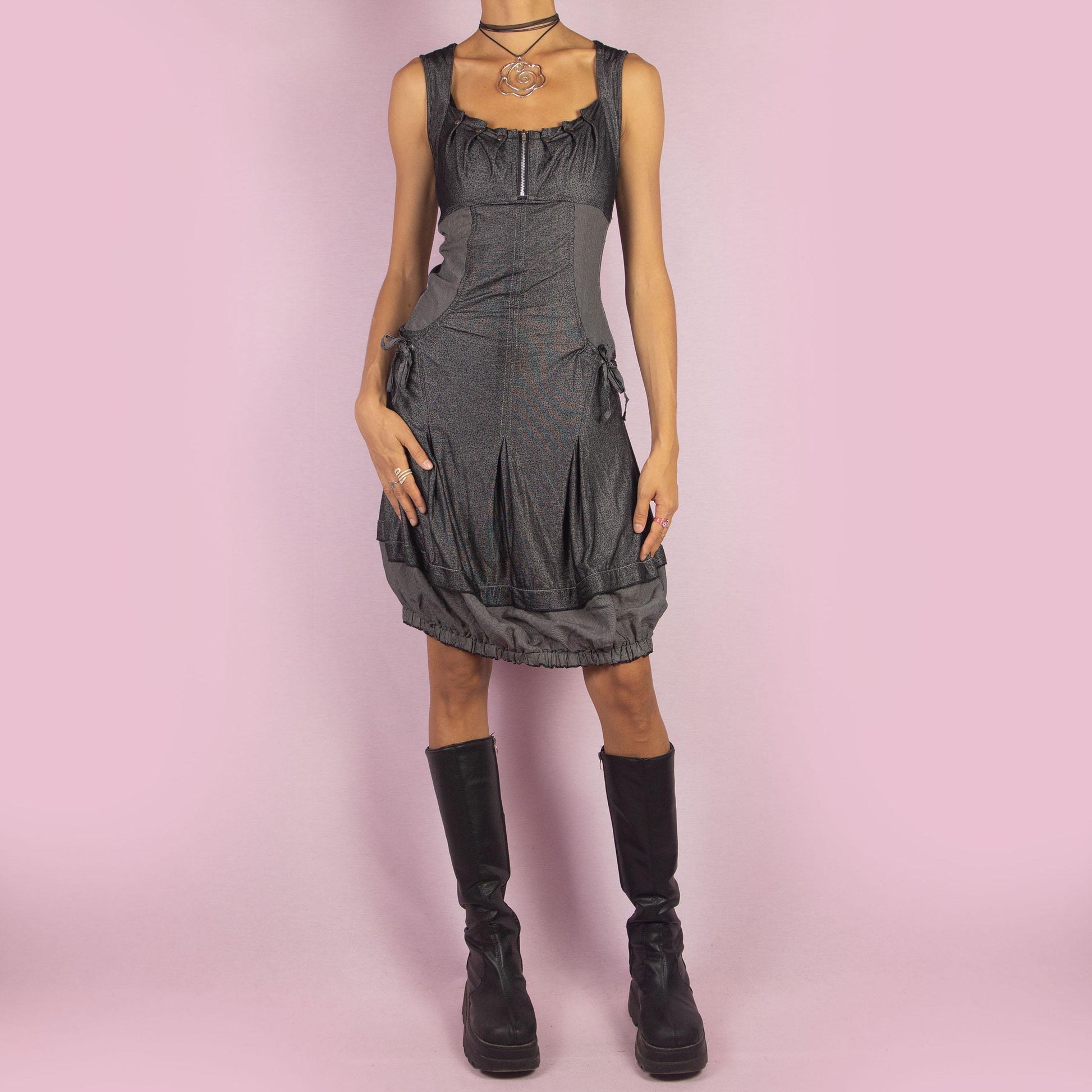 The Y2K Gray Bubble Mini Dress is a vintage 2000s piece featuring a striped, stretchy fabric with a structured bodice and a front zipper detail. The design includes pockets with drawstrings and the bubble hemline adds volume and playfulness.