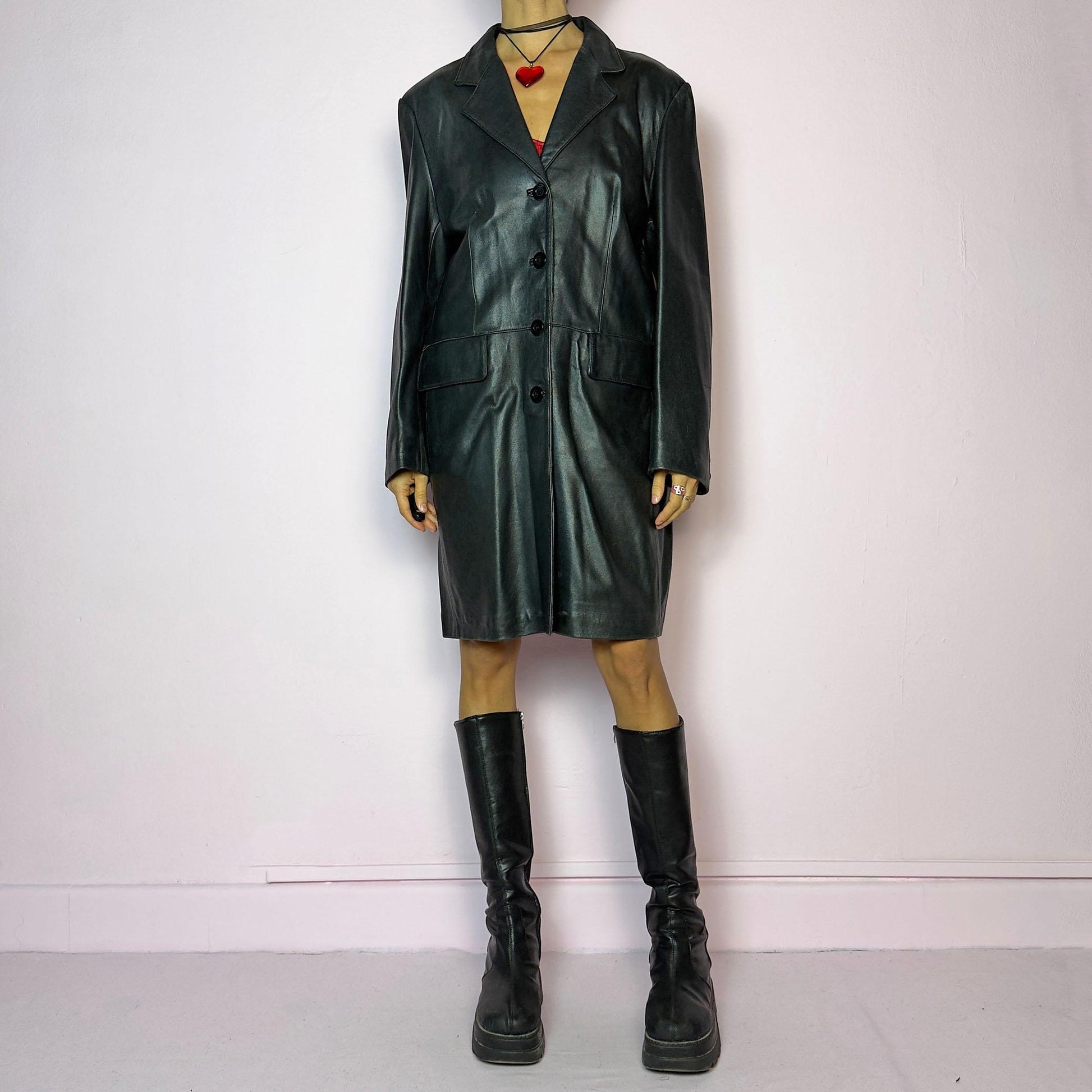 The Vintage 90s Black Leather Coat features a timeless design crafted from genuine black leather, with a button-front closure and a tailored silhouette. Complete with pockets, this versatile coat is ideal for both casual and formal occasions.