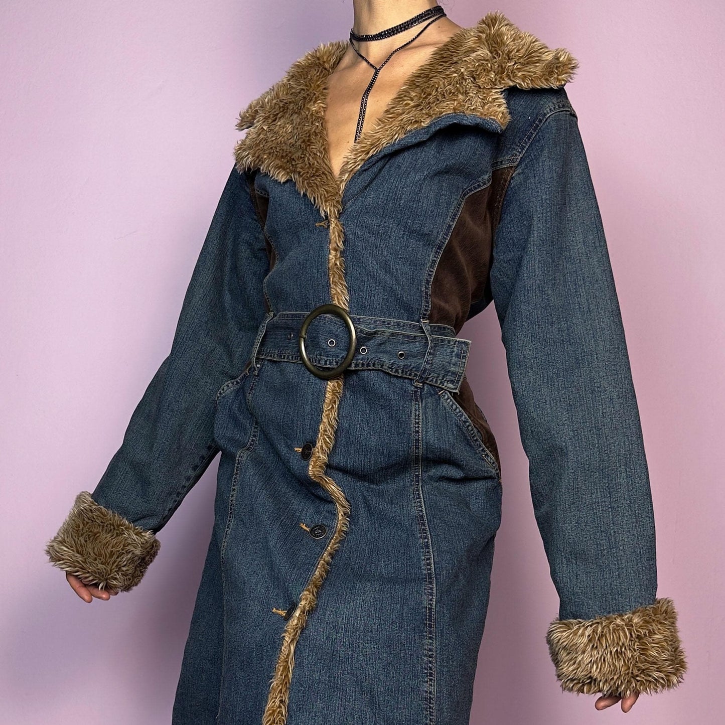 The Y2K Faux Fur Denim Coat is a vintage 2000s piece blending blue denim with cozy brown faux fur trim along the collar, front, cuffs, and hem. It also includes a matching belt with a circular buckle that creates a flattering silhouette