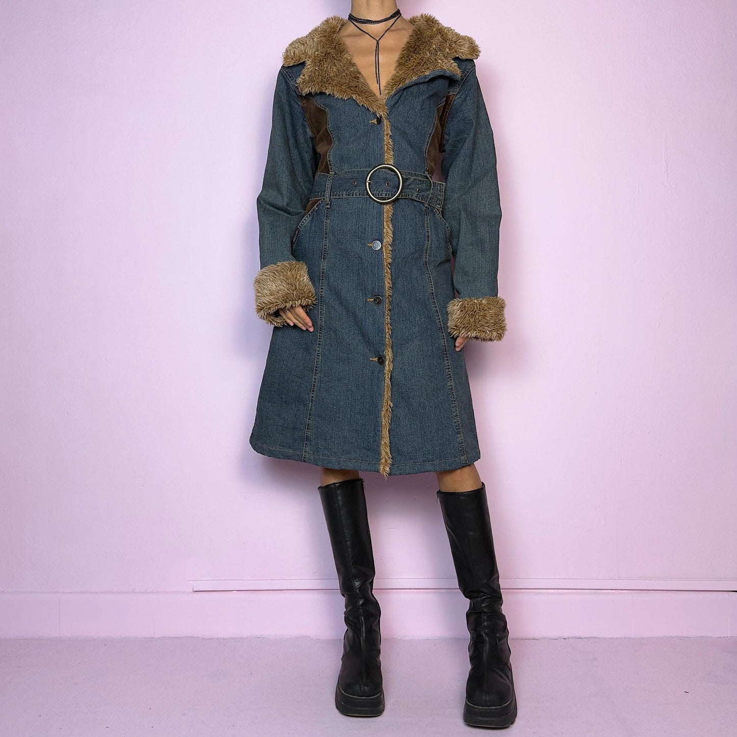 The Y2K Faux Fur Denim Coat is a vintage 2000s piece blending blue denim with cozy brown faux fur trim along the collar, front, cuffs, and hem. It also includes a matching belt with a circular buckle that creates a flattering silhouette