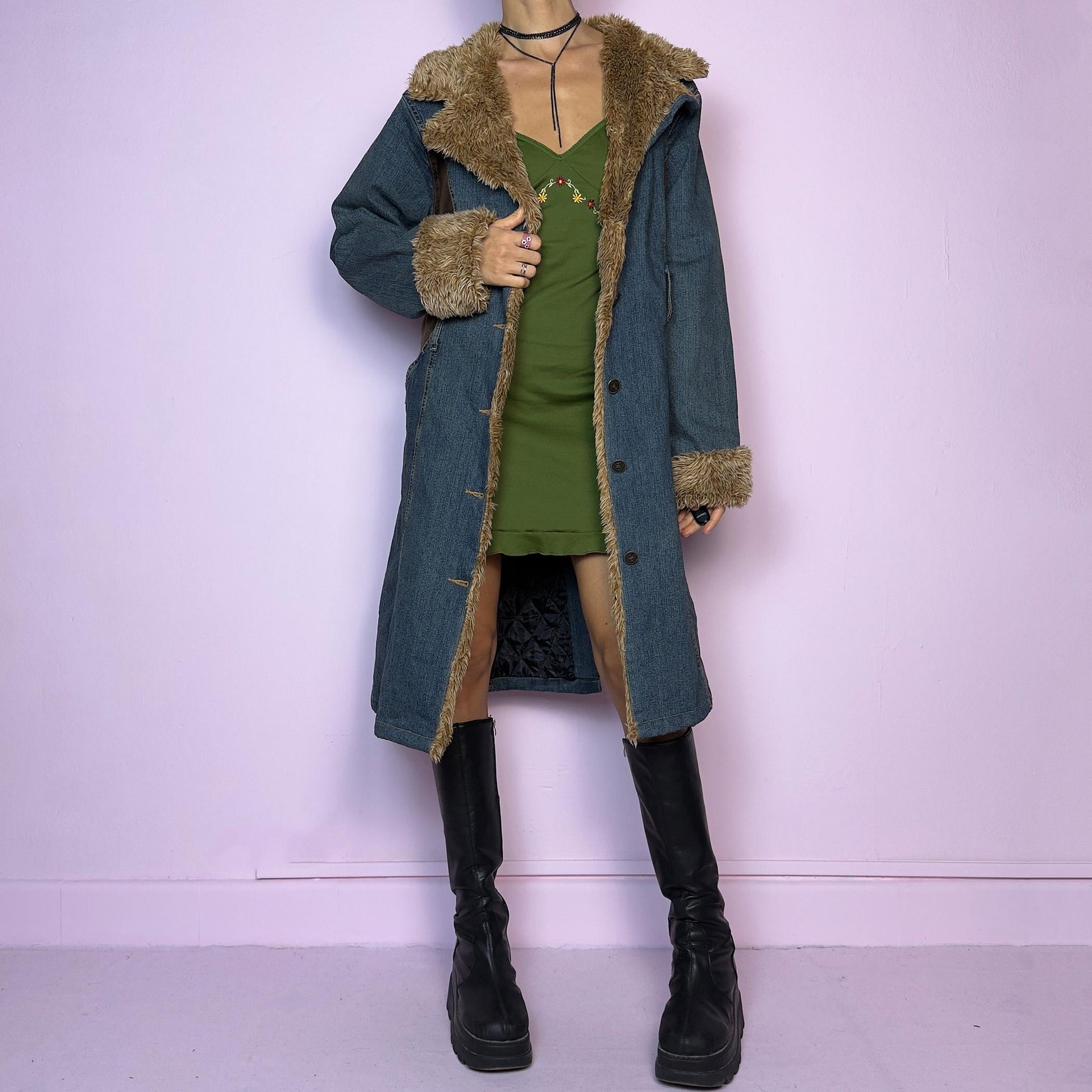 The Y2K Faux Fur Denim Coat is a vintage 2000s piece blending blue denim with cozy brown faux fur trim along the collar, front, cuffs, and hem. It also includes a matching belt with a circular buckle that creates a flattering silhouette