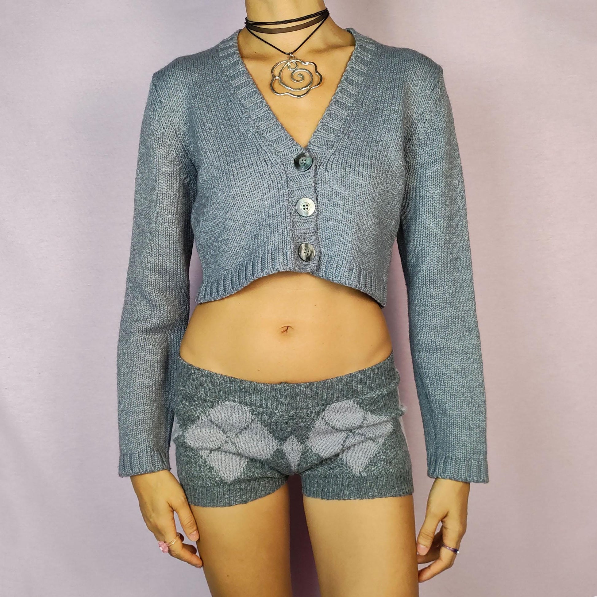 The Y2K Gray Cropped Cardigan is a vintage 2000s sweater featuring a classic V-neck design with a button-front closure, long sleeves, and ribbed detailing on the hem and cuffs. Crafted from a merino wool and acrylic blend