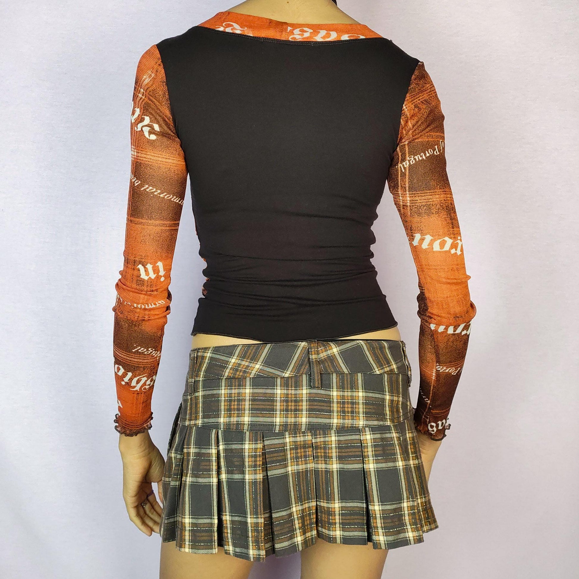 The Y2K Print Mesh Wrap Top is a vintage 2000s piece featuring a vibrant orange and brown design with bold typography prints. Crafted from a lightweight mesh fabric, it has a wrap-style front that accentuates the silhouette and long sleeves