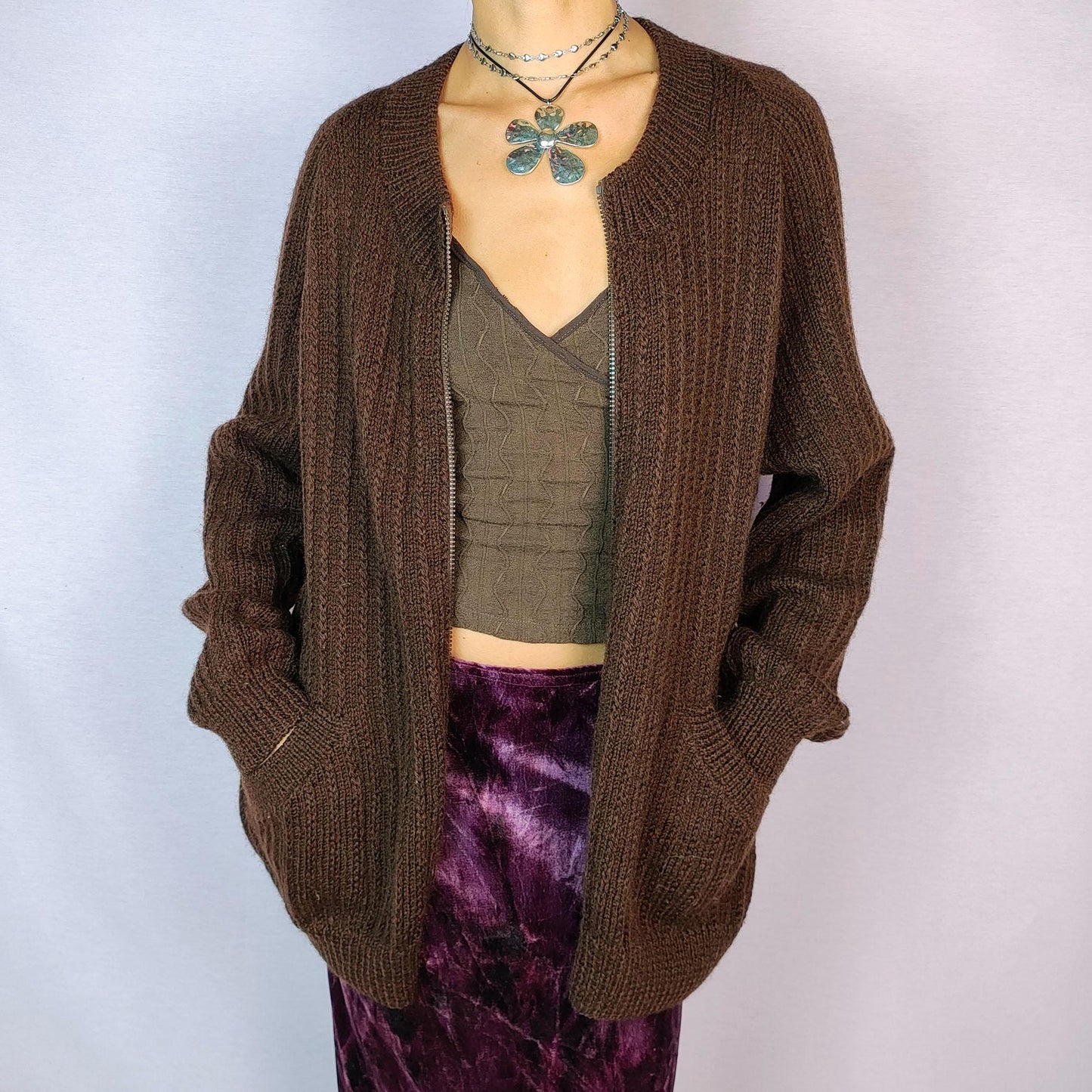 The Vintage 90s Brown Zip Cardigan features a relaxed fit with a ribbed knit design, full front zipper closure, and two pockets for a functional yet cozy style. Crafted in a dark warm brown tone, this versatile piece is perfect for layering