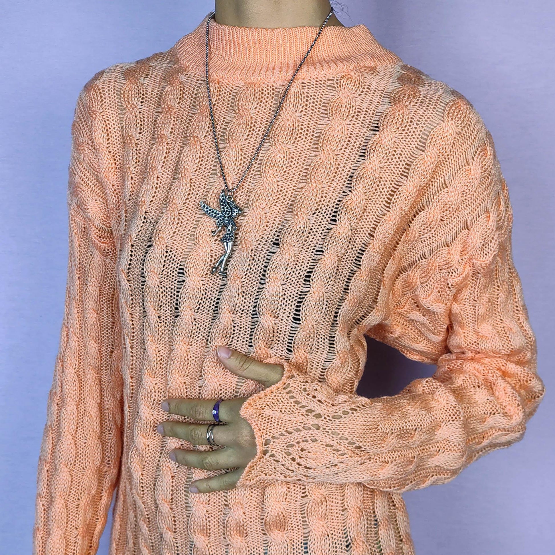 The Vintage 90s Peach Knit Sweater features a soft knit design with an openwork cable pattern, delicate scalloped hem detailing, long sleeves and a mock neckline. This lightweight sweater is crafted in a warm peach tone. Adult World Shop.