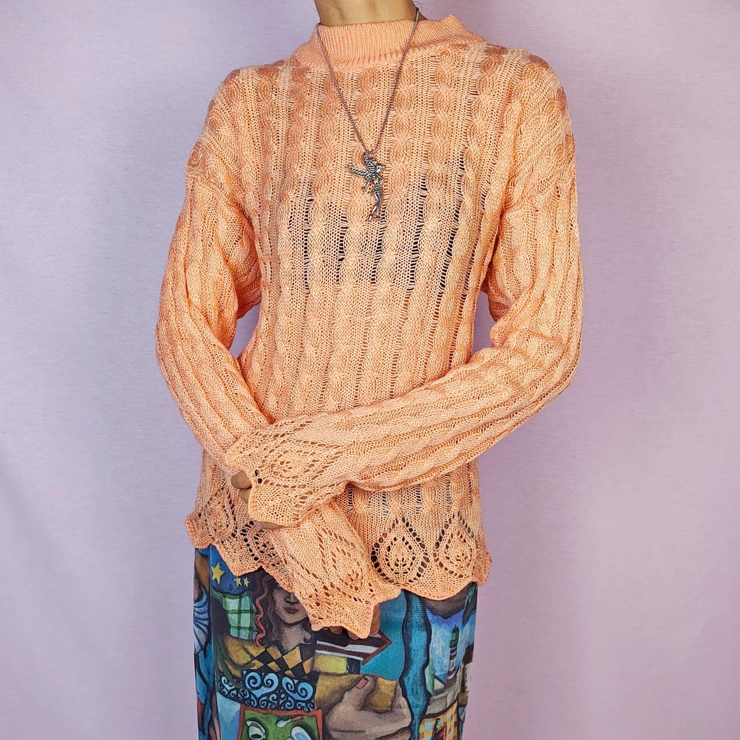 The Vintage 90s Peach Knit Sweater features a soft knit design with an openwork cable pattern, delicate scalloped hem detailing, long sleeves and a mock neckline. This lightweight sweater is crafted in a warm peach tone. Adult World Shop.