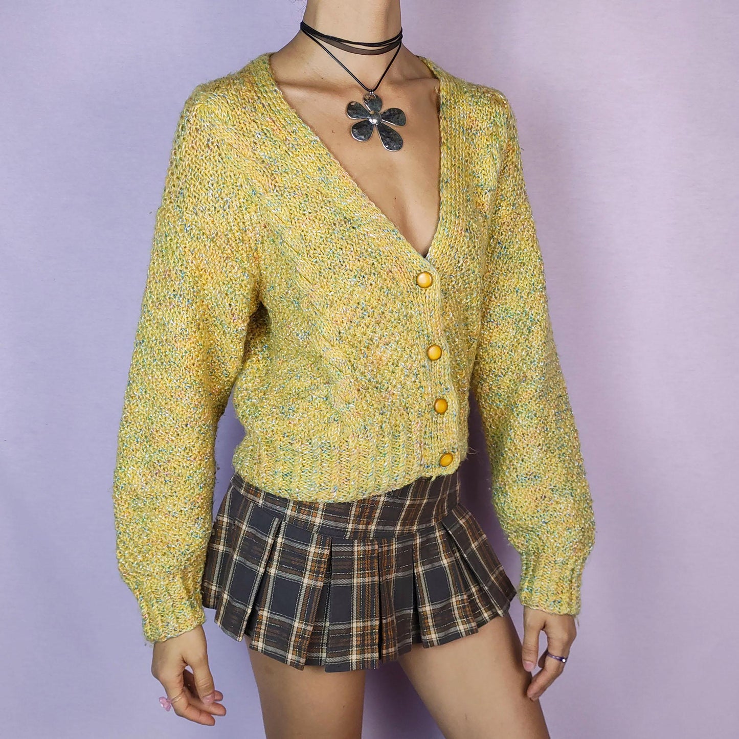 The Vintage 90s Yellow Knit Cardigan is a cozy and vibrant sweater featuring a chunky knit design in a cheerful yellow hue with flecks of multicolored yarn for added texture. This cardigan is styled with a V-neckline, button closure, and ribbed hem