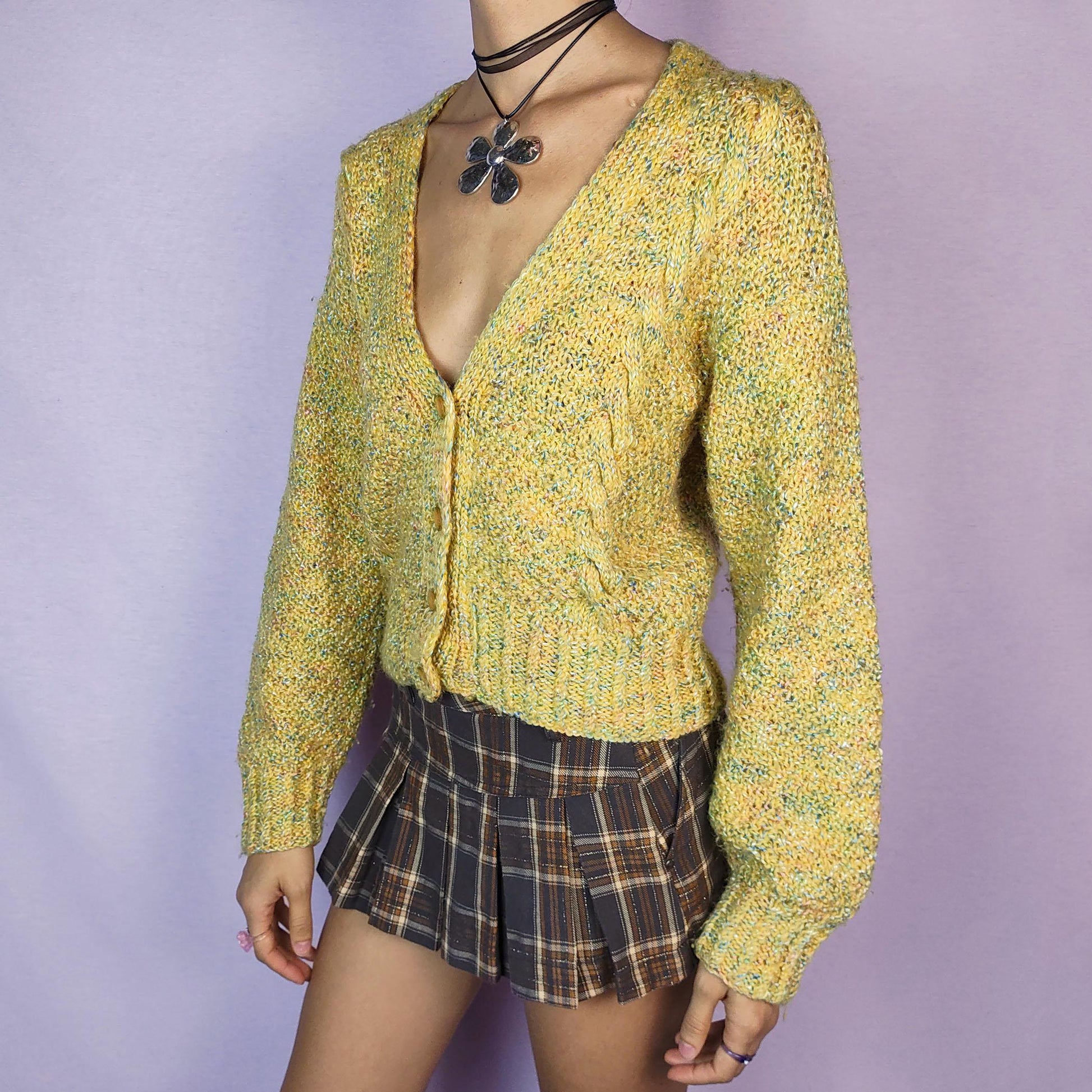 The Vintage 90s Yellow Knit Cardigan is a cozy and vibrant sweater featuring a chunky knit design in a cheerful yellow hue with flecks of multicolored yarn for added texture. This cardigan is styled with a V-neckline, button closure, and ribbed hem