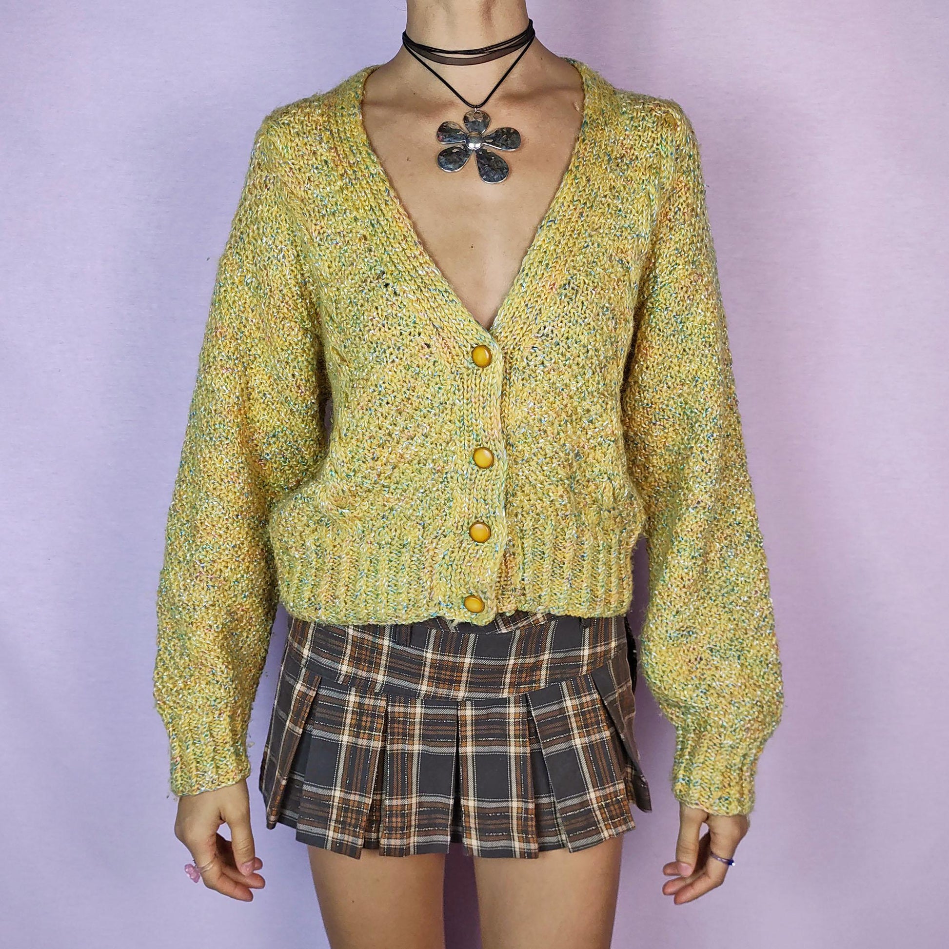 The Vintage 90s Yellow Knit Cardigan is a cozy and vibrant sweater featuring a chunky knit design in a cheerful yellow hue with flecks of multicolored yarn for added texture. This cardigan is styled with a V-neckline, button closure, and ribbed hem