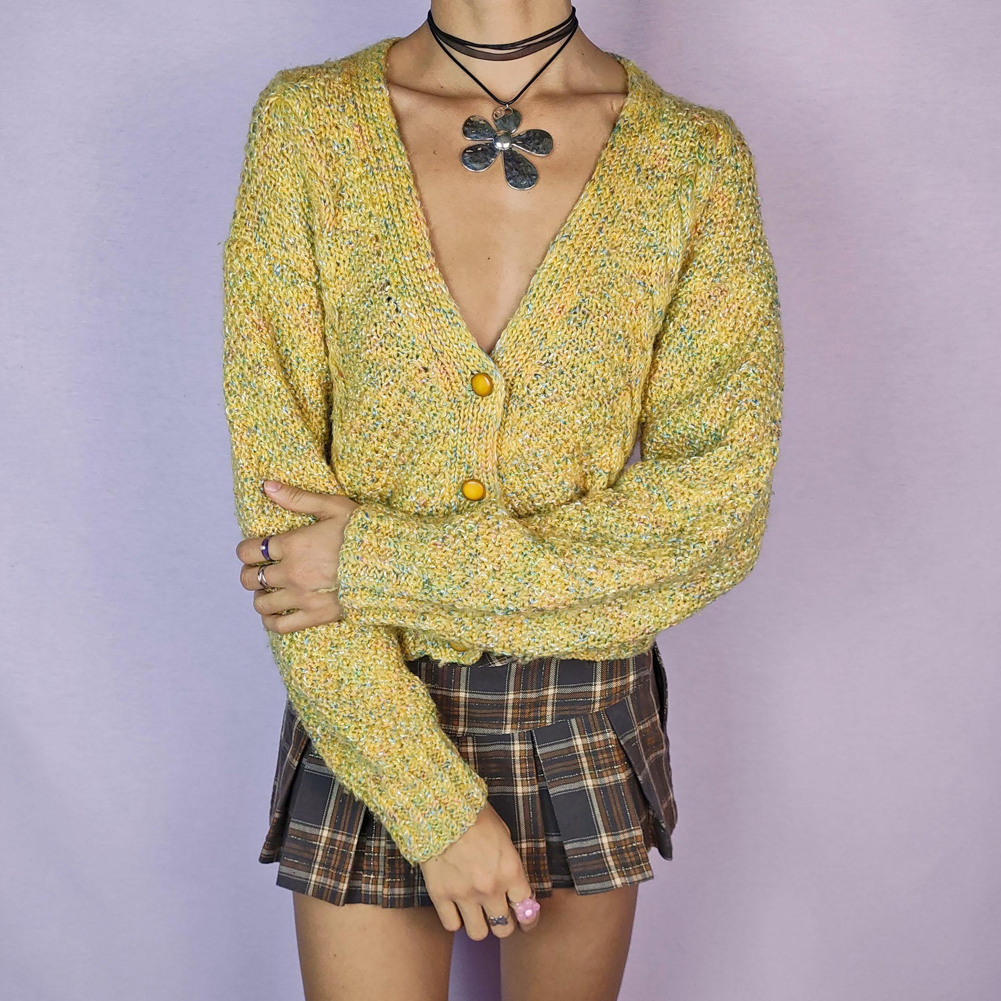 The Vintage 90s Yellow Knit Cardigan is a cozy and vibrant sweater featuring a chunky knit design in a cheerful yellow hue with flecks of multicolored yarn for added texture. This cardigan is styled with a V-neckline, button closure, and ribbed hem