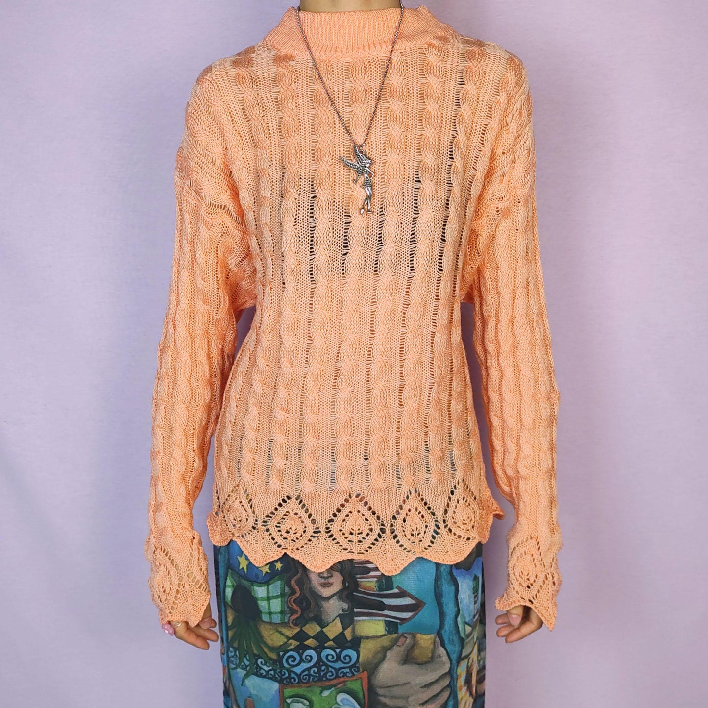 The Vintage 90s Peach Knit Sweater features a soft knit design with an openwork cable pattern, delicate scalloped hem detailing, long sleeves and a mock neckline. This lightweight sweater is crafted in a warm peach tone. Adult World Shop.